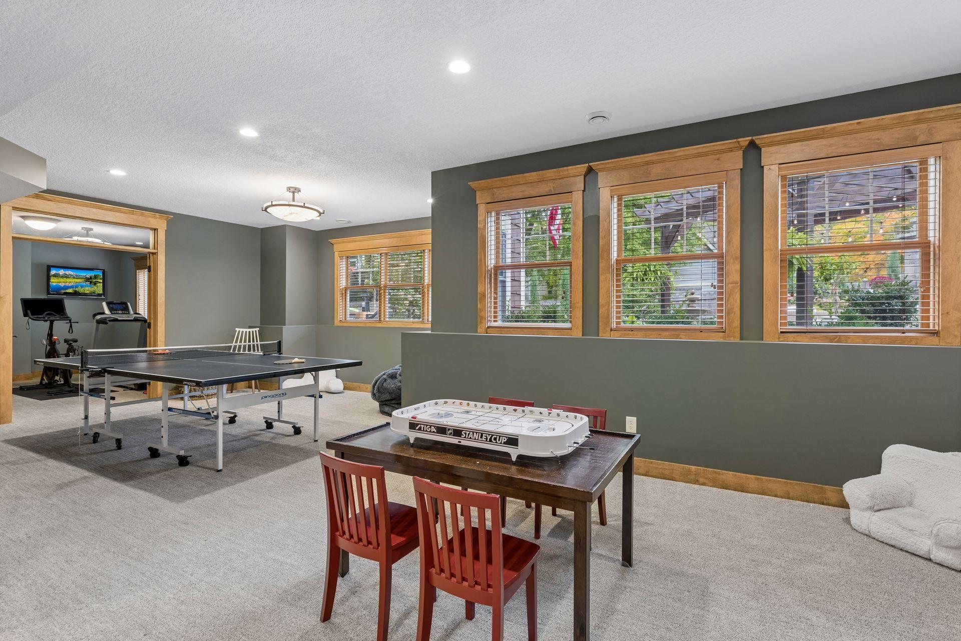 Basement game room with ping-pong and tabletop hockey games, exercise equipment, and large windows.