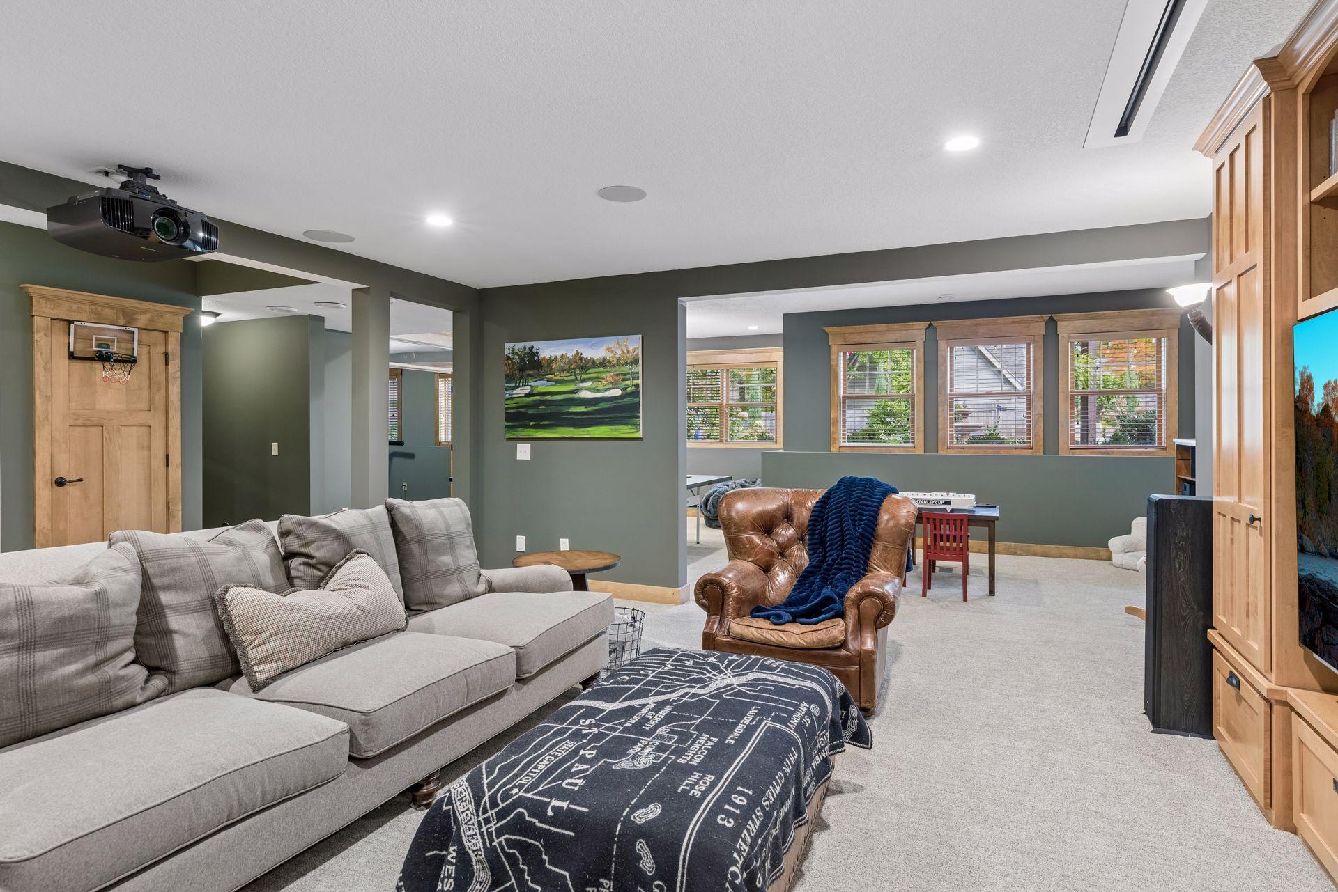 Family room with a ceiling-mounted projector, gray sectional, leather chair, and built-in wooden cabinetry.