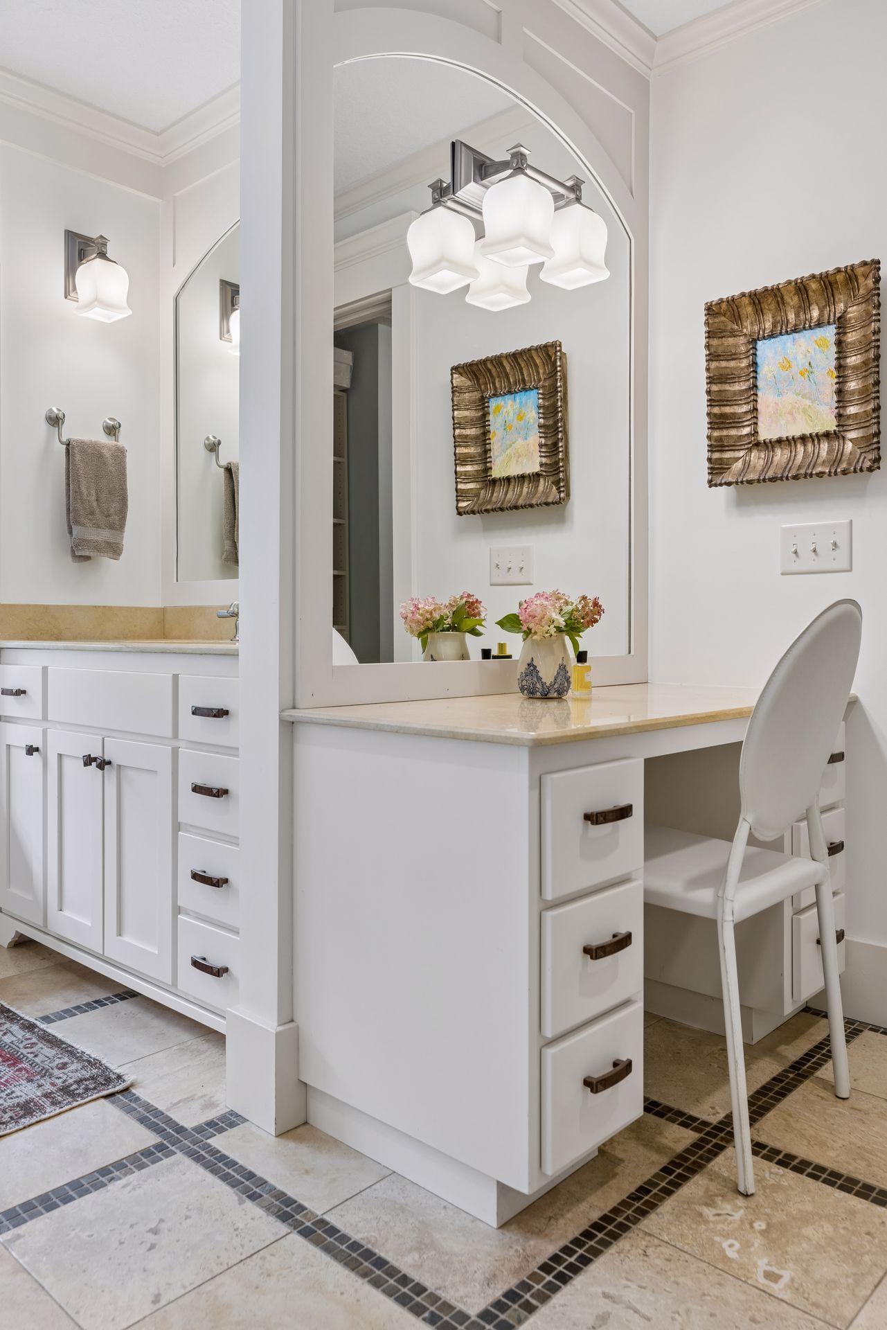 Bright bathroom with white vanity cabinets, an arched mirror, and a tiled floor with mosaic borders.