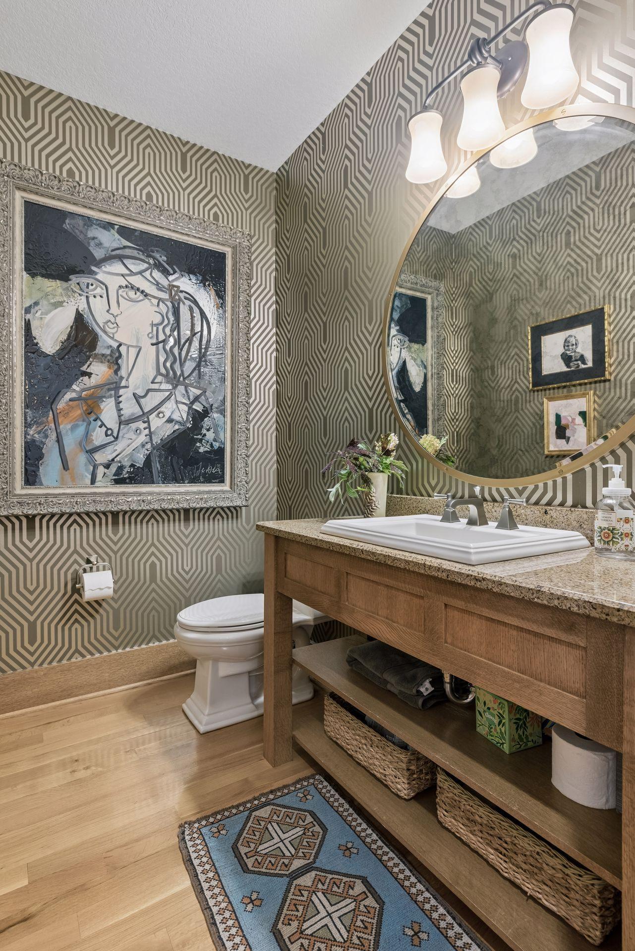 Powder room with geometric wallpaper, wood vanity, oval mirror, and framed artwork.