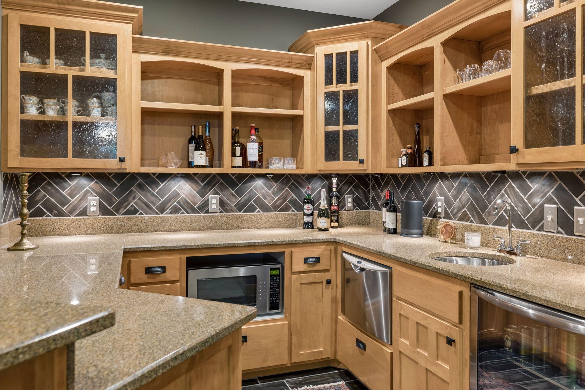 Wet bar with light wood cabinets, granite counters, herringbone tile backsplash, sink, and wine refrigerator.