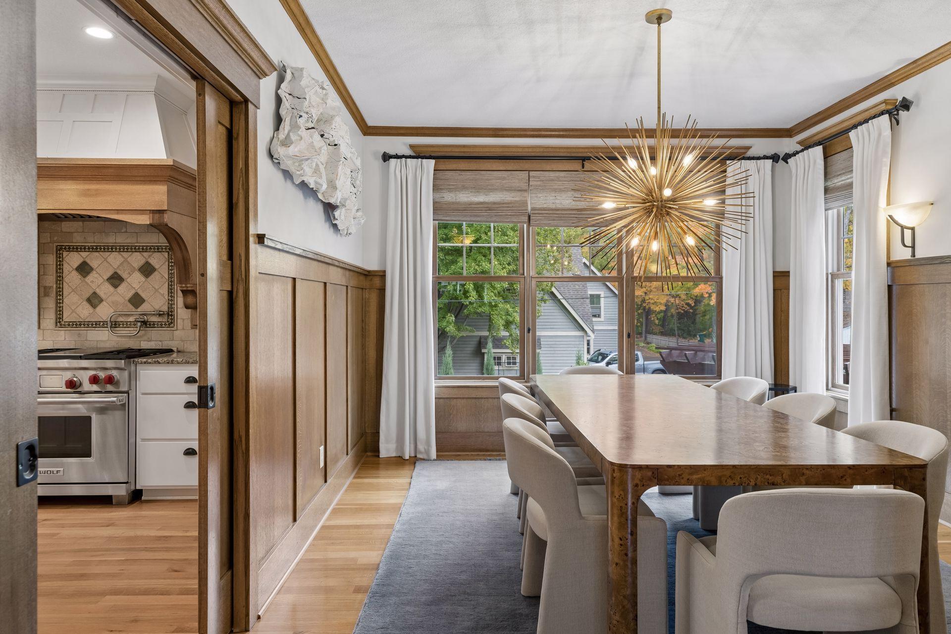 Dining room with wood paneling, a long table, starburst chandelier, and large windows.
