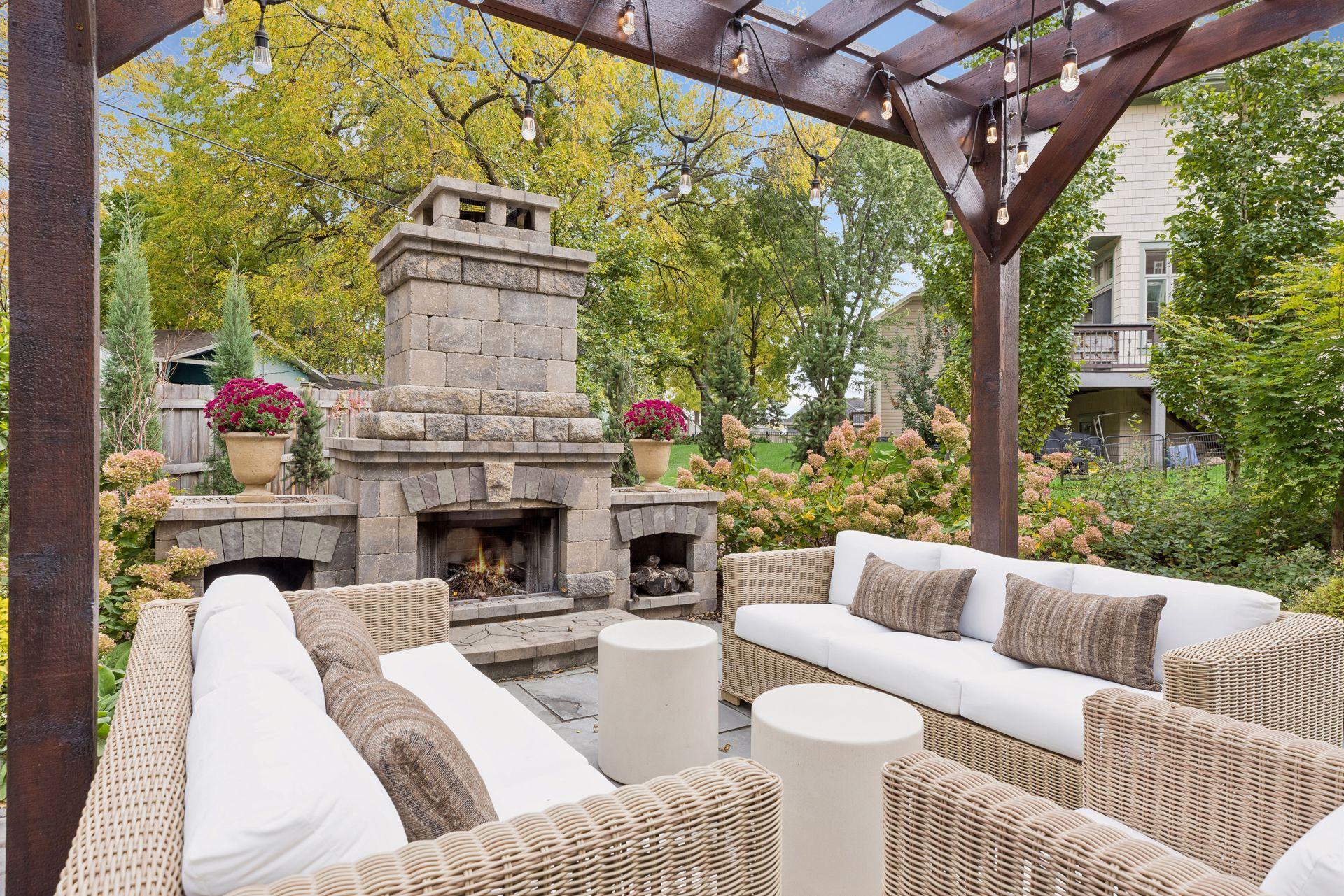Patio with wicker seating, a stone fireplace, and string lights beneath a pergola.