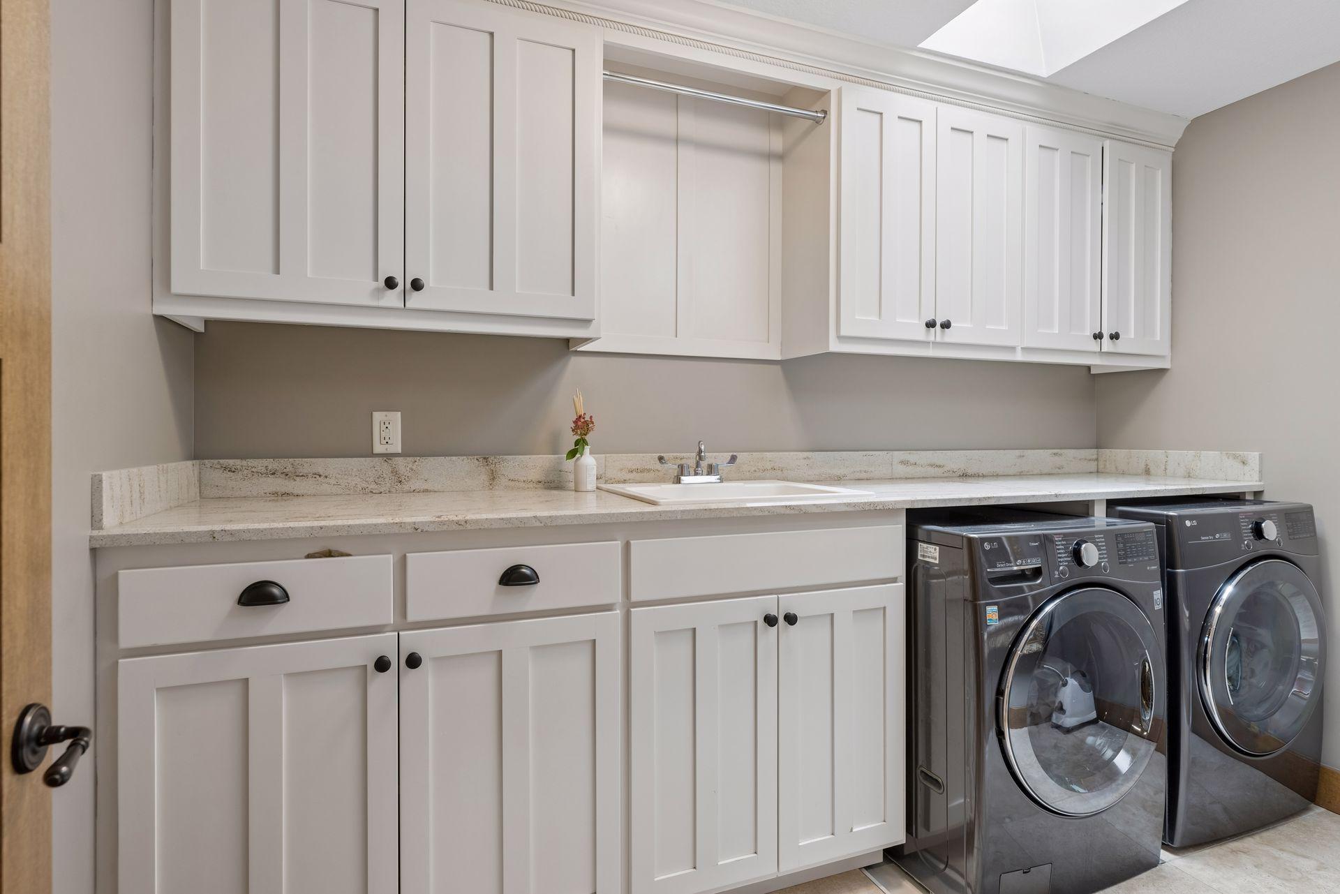 Laundry room with white cabinets, a stone counter and sink, and front-loading washer and dryer.