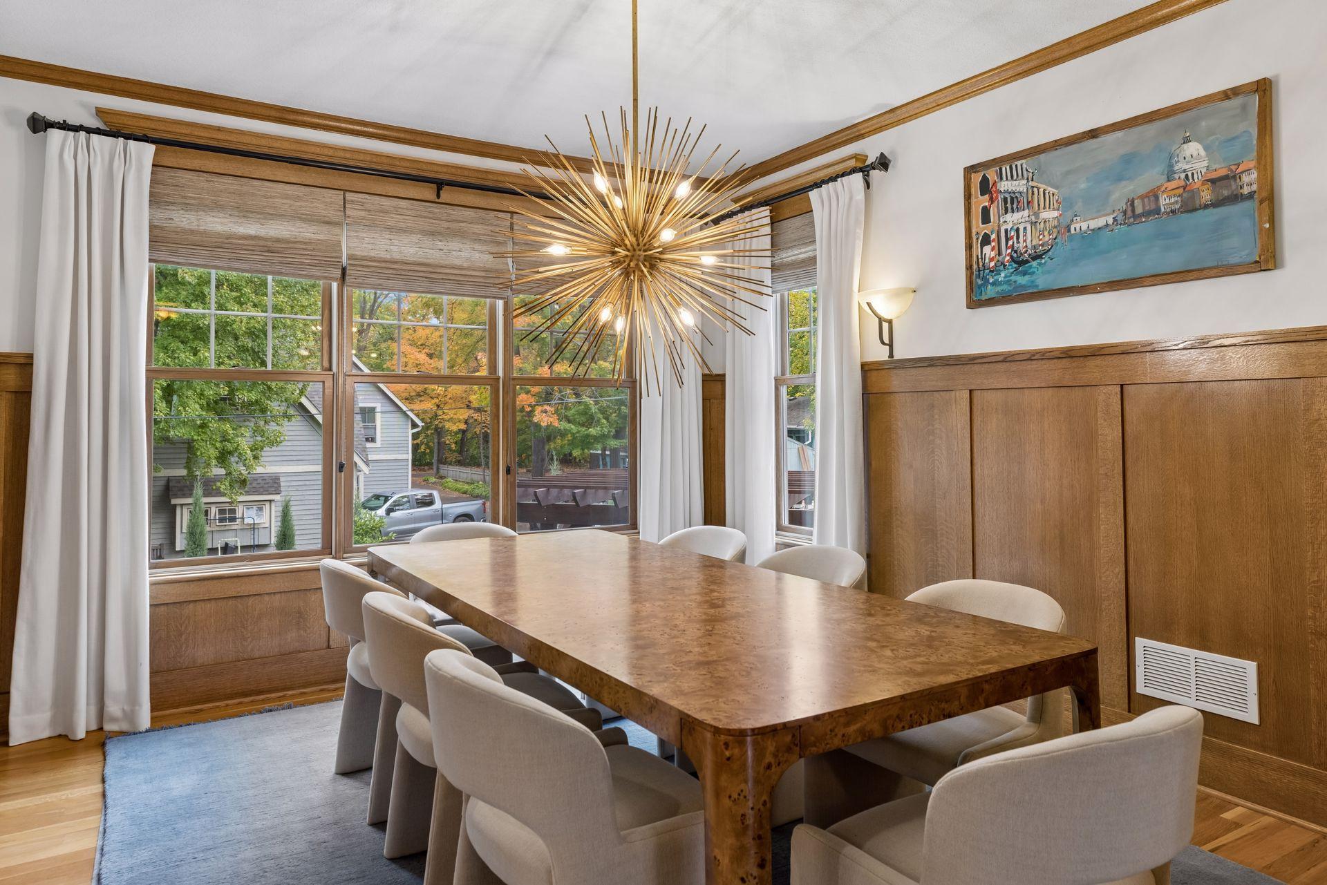 Dining room with a wood table, paneled walls, tall windows, and a gold starburst chandelier.