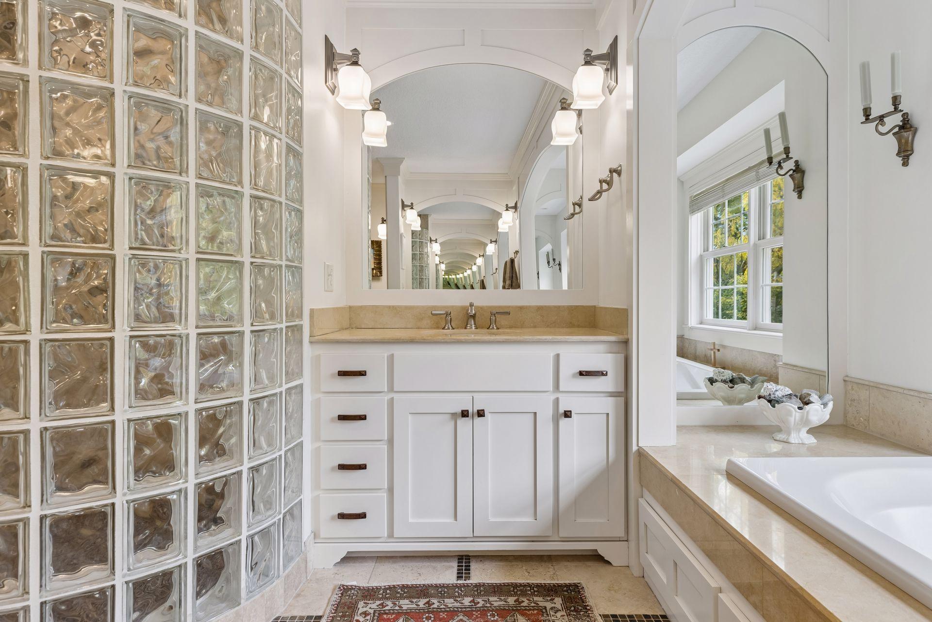 Bathroom vanity and bathtub with a glass-block wall, arched openings, and a window.