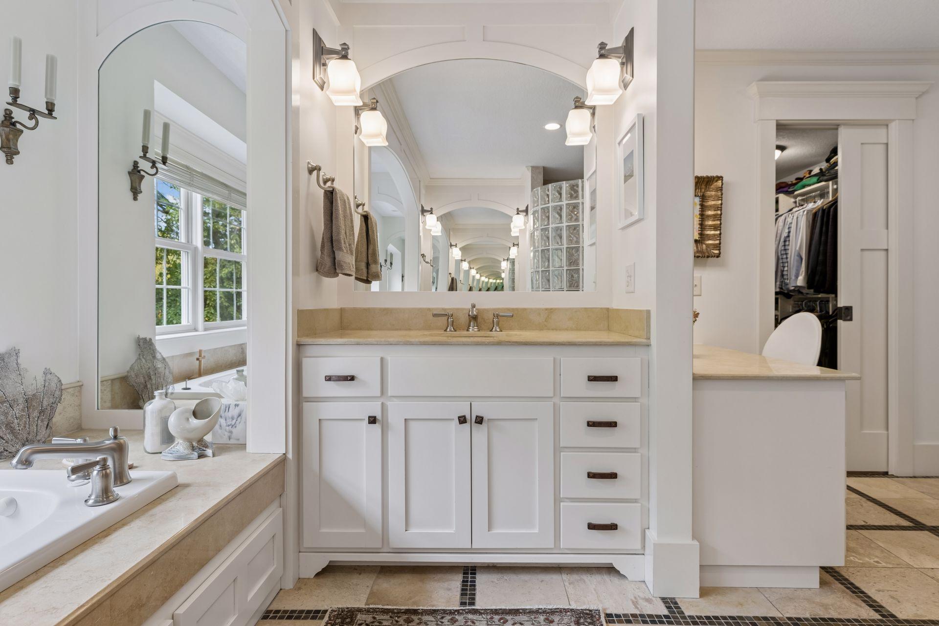 Bathroom with a long white vanity, expansive mirrors, and an adjoining walk-in closet.