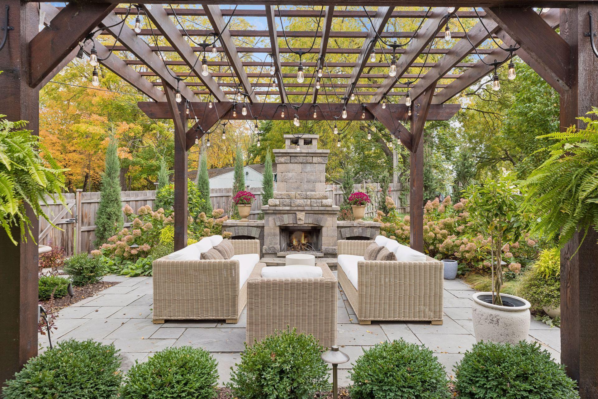 Outdoor patio with wicker seating, a stone fireplace, and a timber pergola strung with lights.