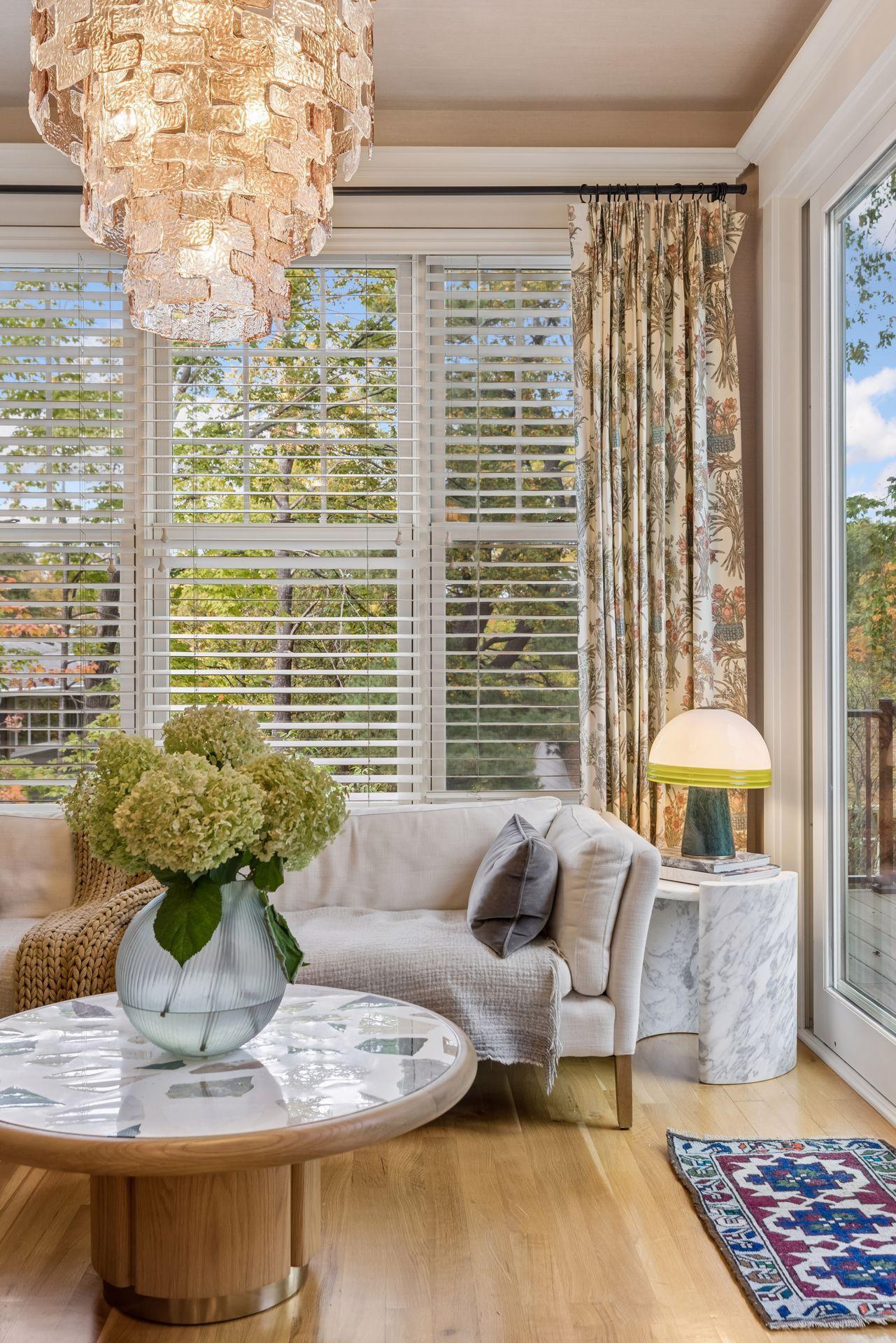 Living room with a white sofa, large windows, sculptural chandelier, and round marble-topped coffee table.