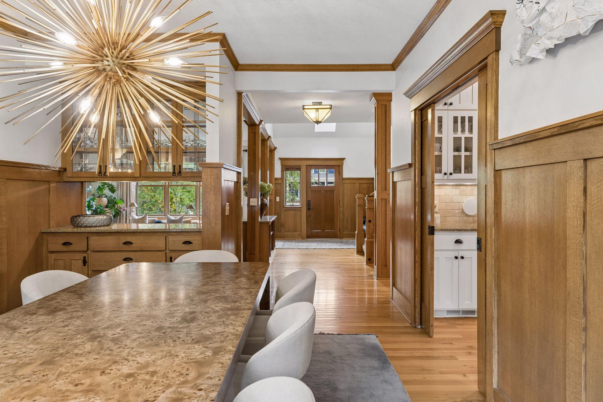 Dining area with a stone-topped table and brass starburst chandelier, opening onto a wood-paneled hallway.