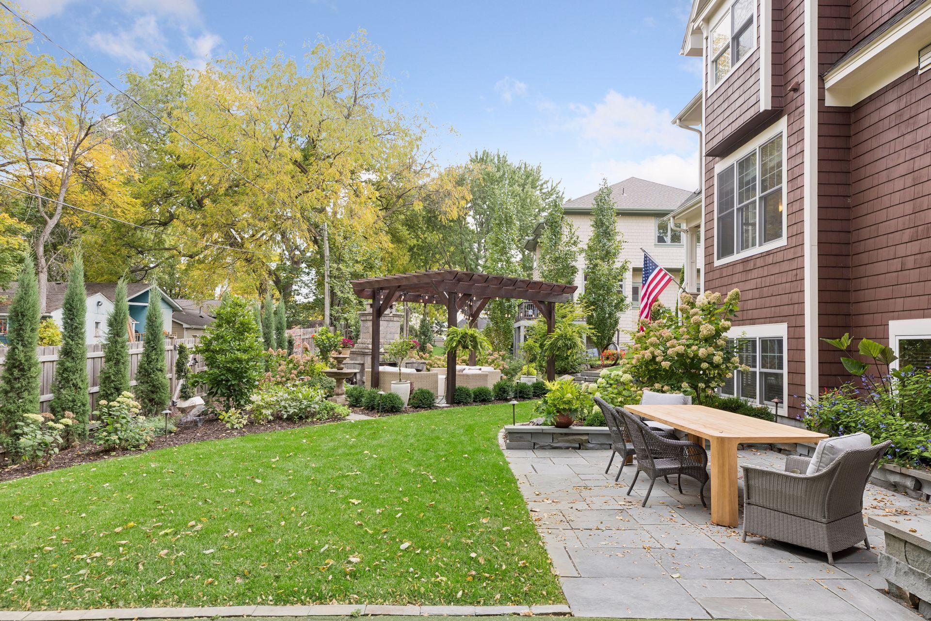 Backyard with a stone patio, outdoor dining set, wooden pergola, and landscaped lawn.