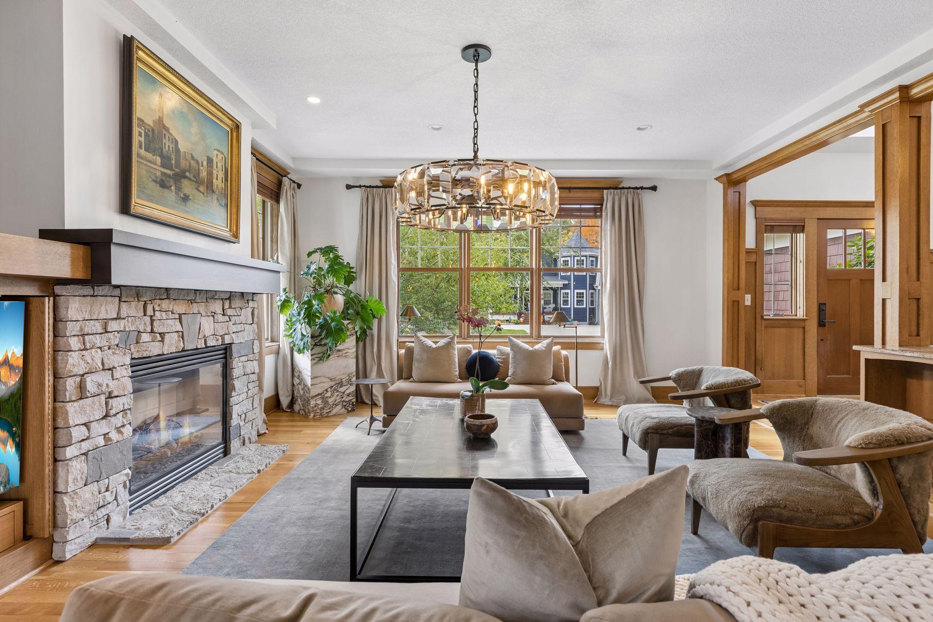 Living room with a stone fireplace, large windows, and a faceted chandelier.
