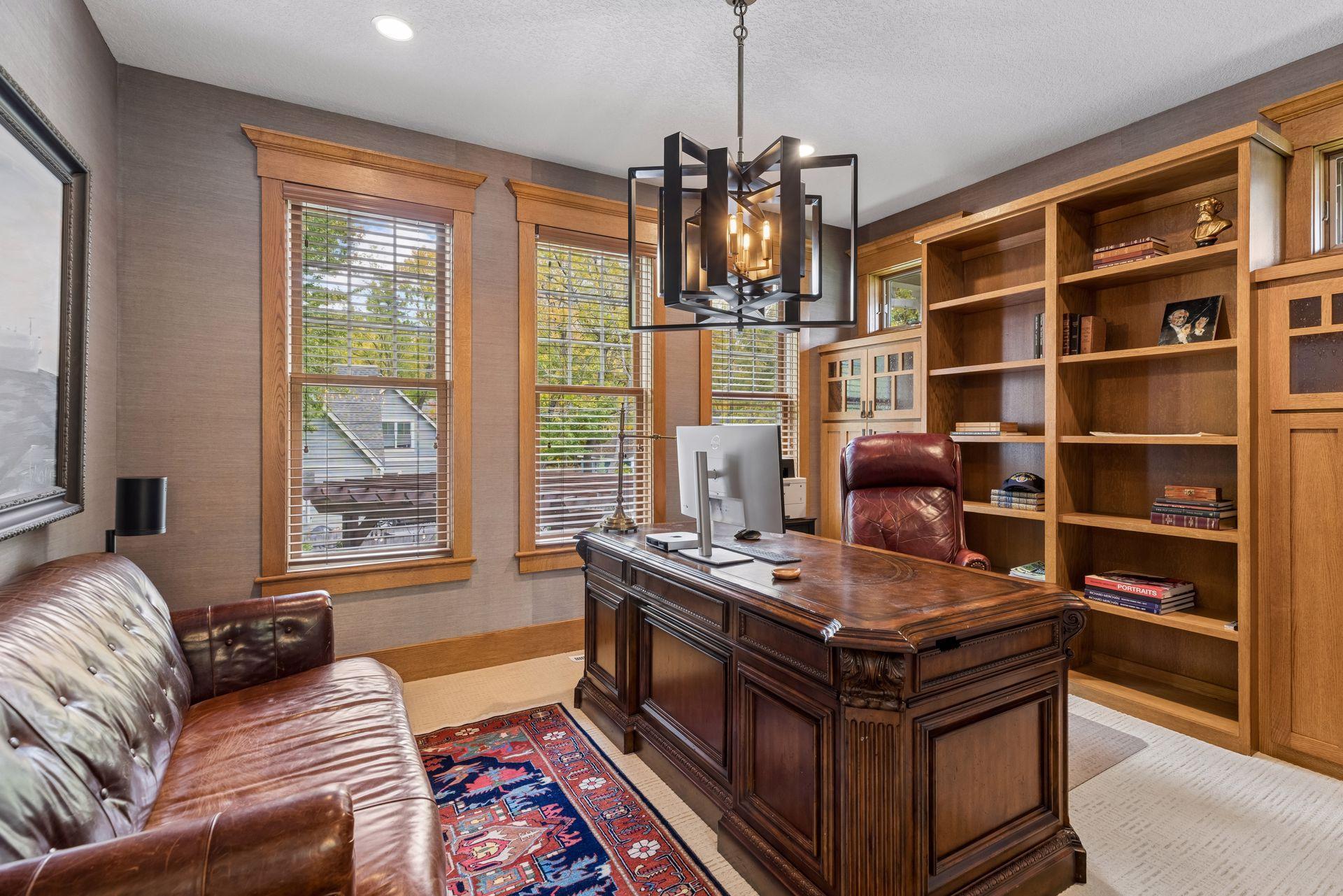 Home office with a carved wood desk, built-in bookcases, and tall windows.