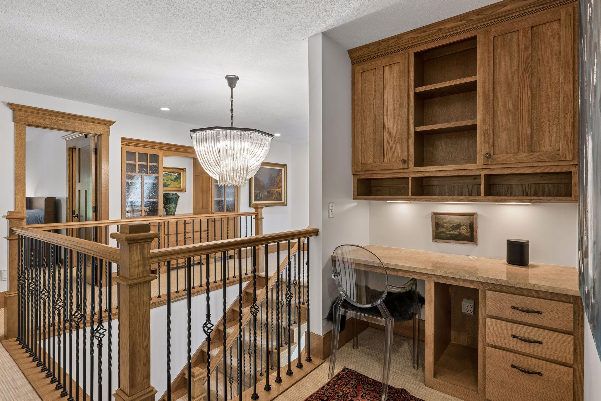 Upstairs desk nook with oak cabinetry and stone countertop beside a wood-and-iron stair railing.