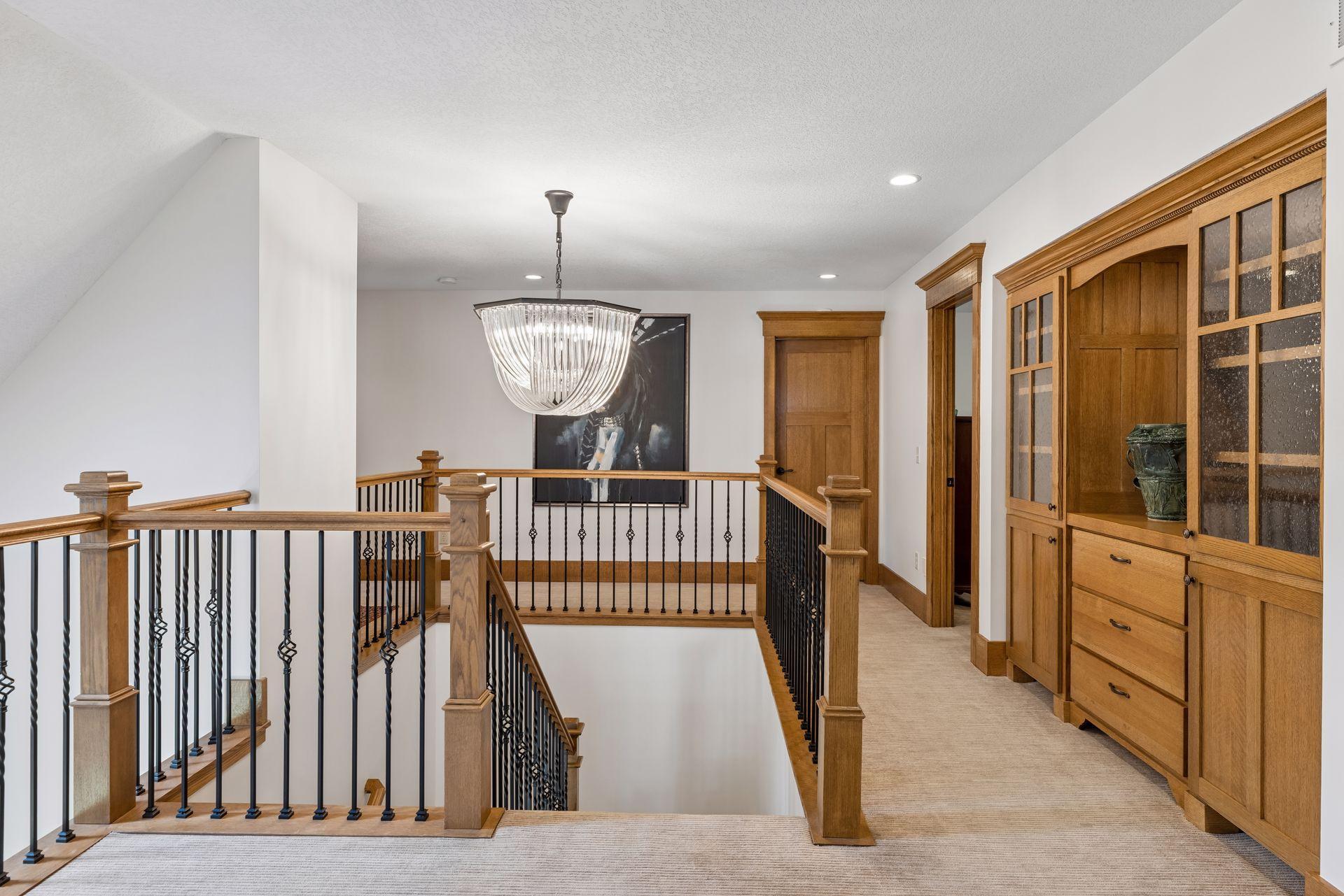 Upstairs landing overlooking a staircase, with wood railings, a glass chandelier, and built-in cabinetry.