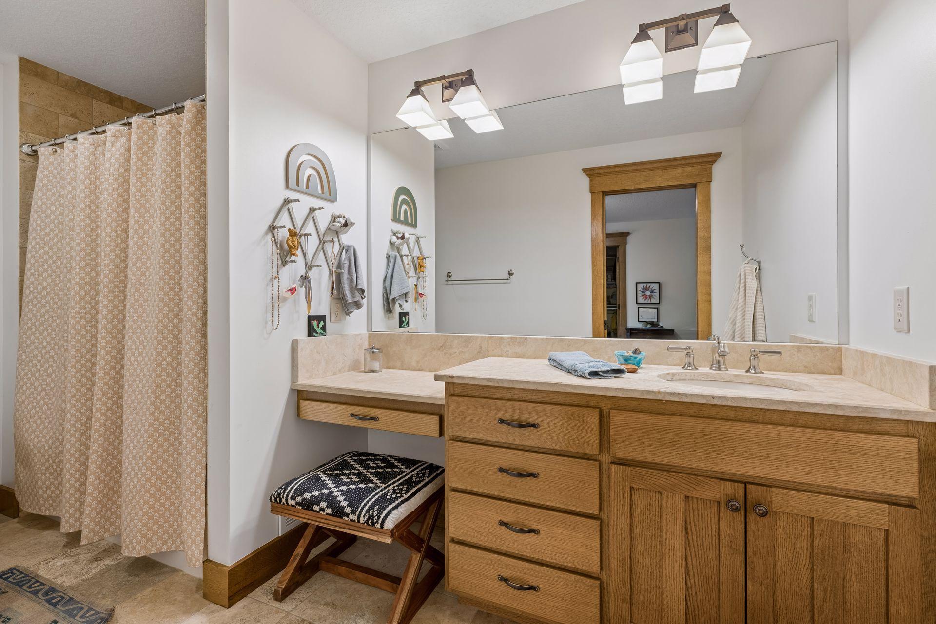 Bathroom with a wide oak vanity and a tiled shower behind a patterned curtain.