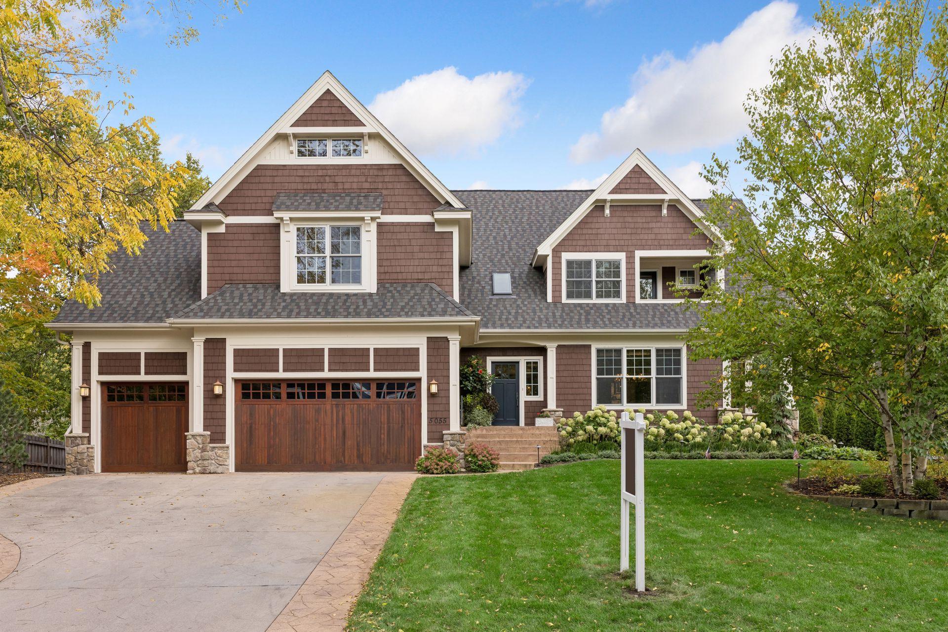 Brown shingle-sided home with multiple gables, three wood garage doors, and autumn landscaping.