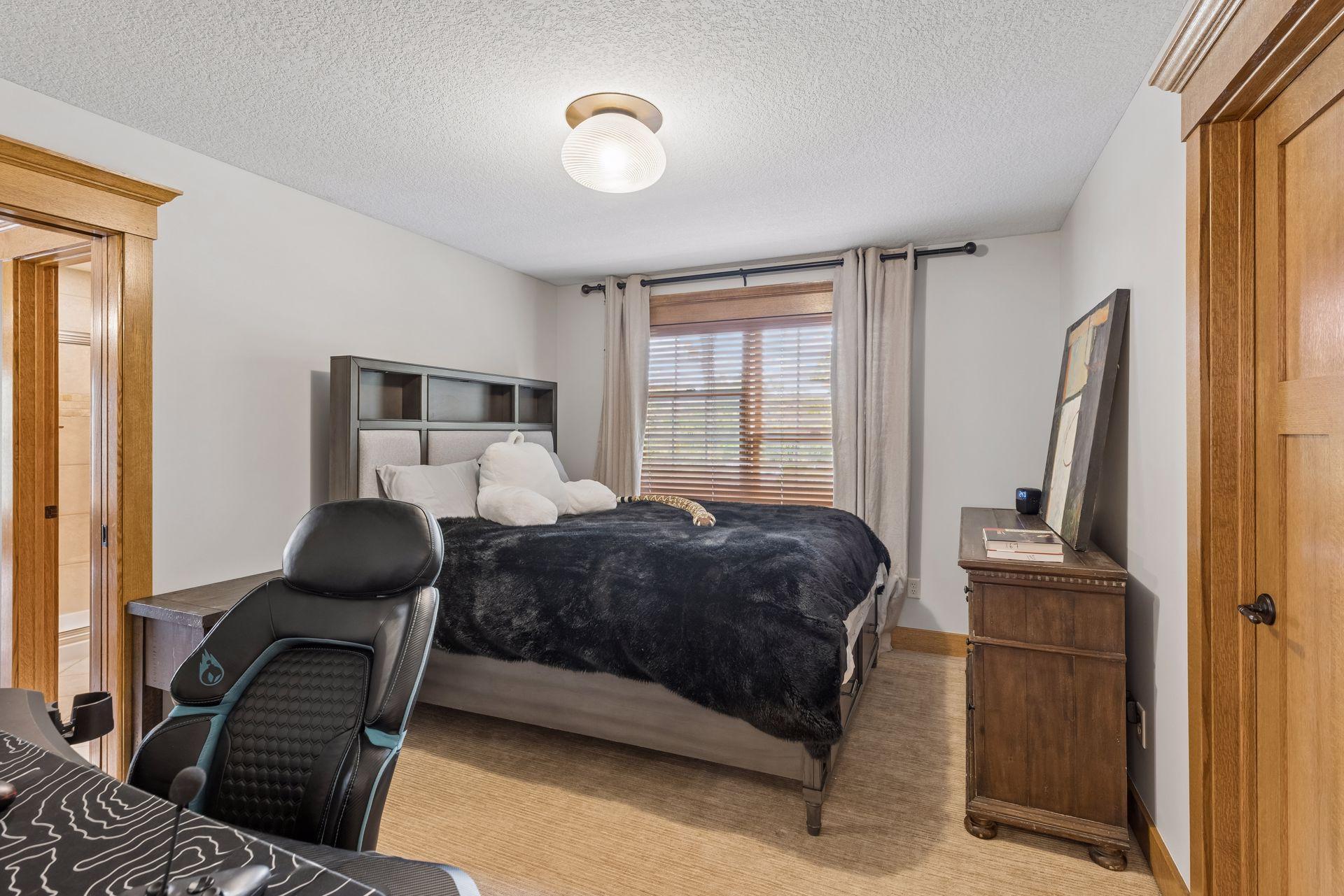Furnished bedroom with a dark bedspread, wood trim, and a window with blinds.