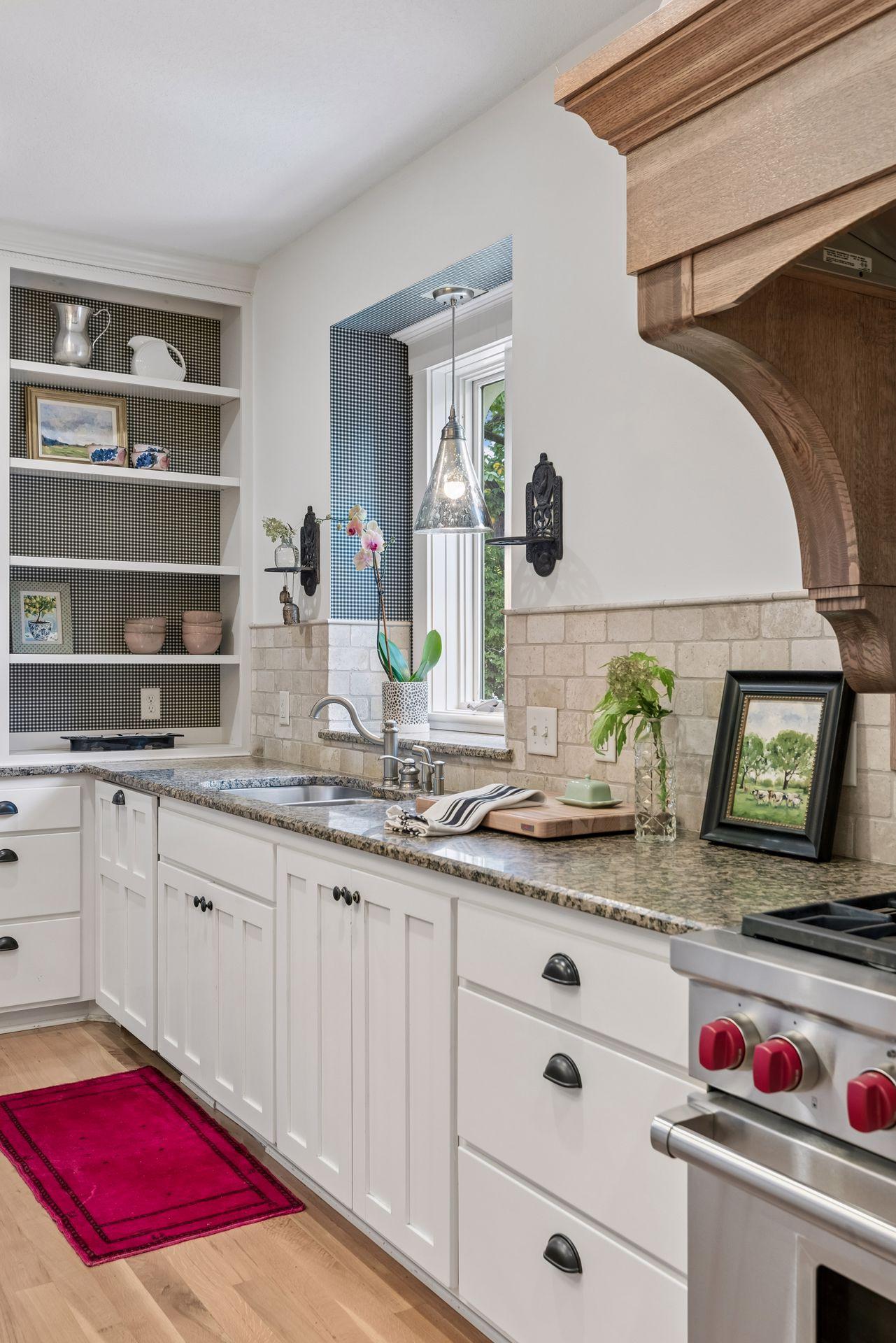 Kitchen with white shaker cabinets, granite counters, patterned open shelves, and a large wood range hood.