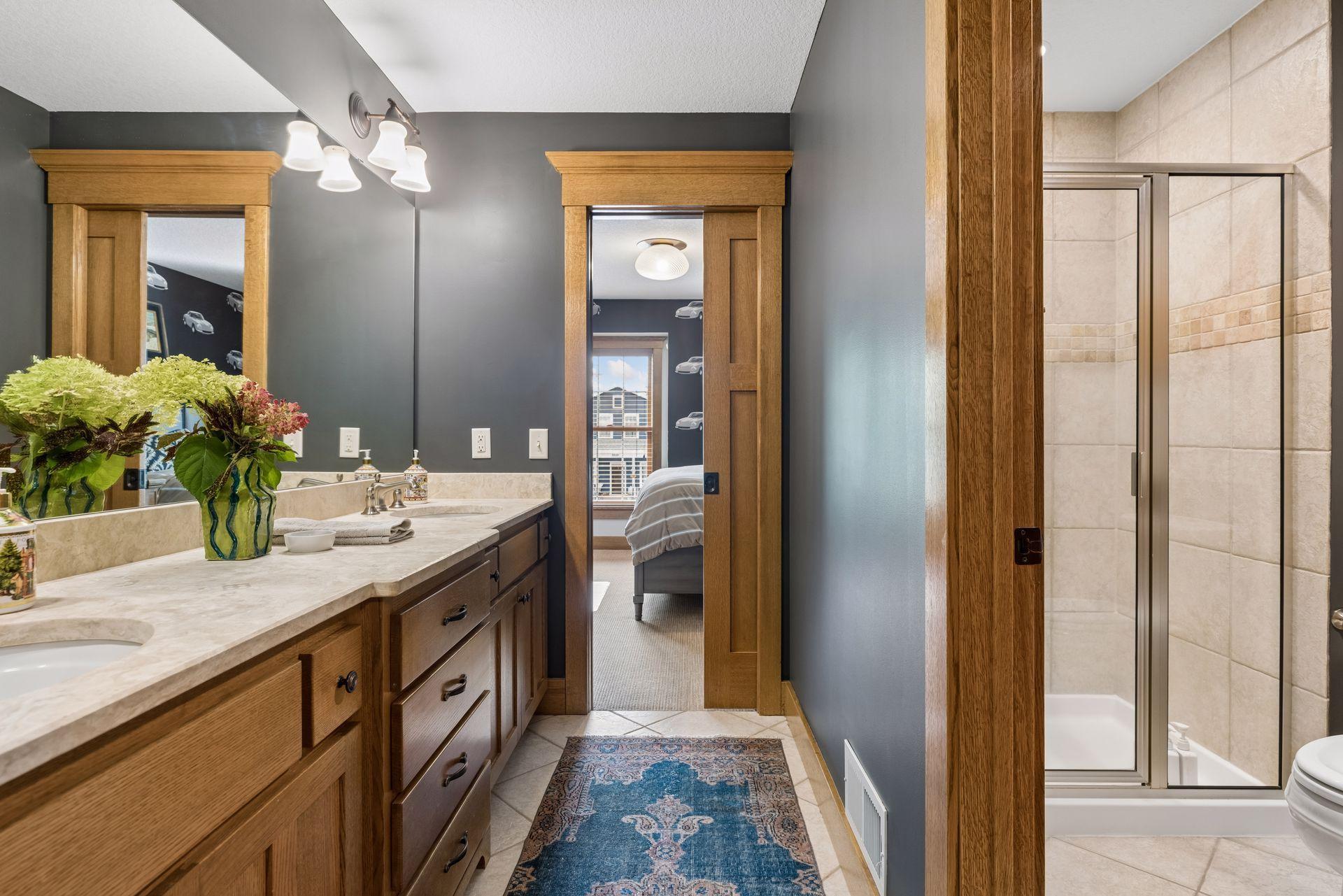 Bathroom with a long wood double vanity, blue runner rug, and tiled tub and shower.