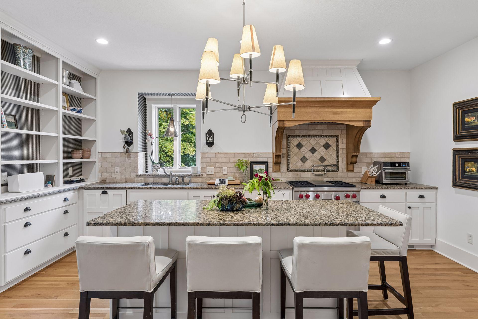 Bright kitchen with a large granite island, white cabinetry, and a prominent wood range hood.