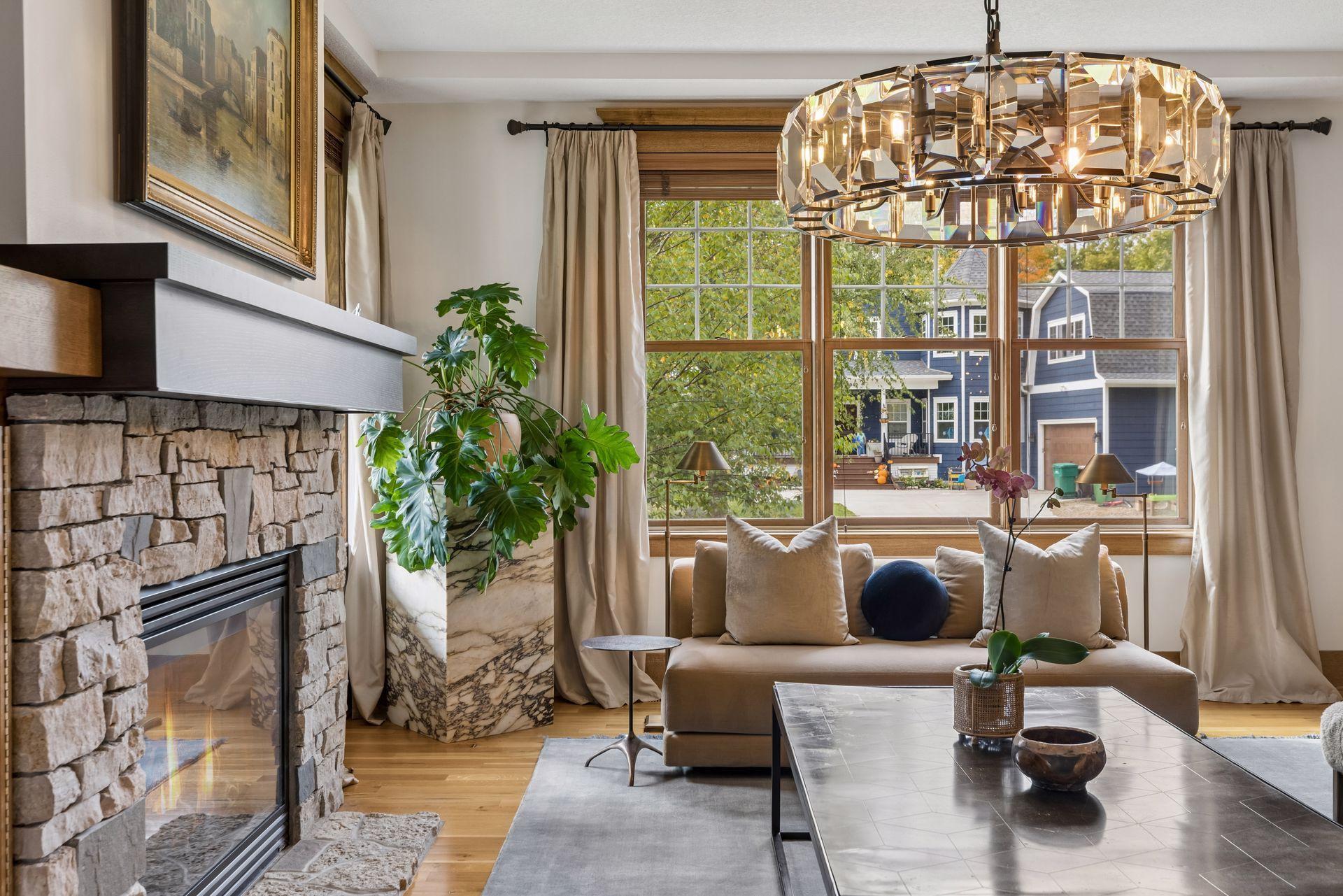 Living room with a stone fireplace, large windows, and a faceted chandelier above the sofa.