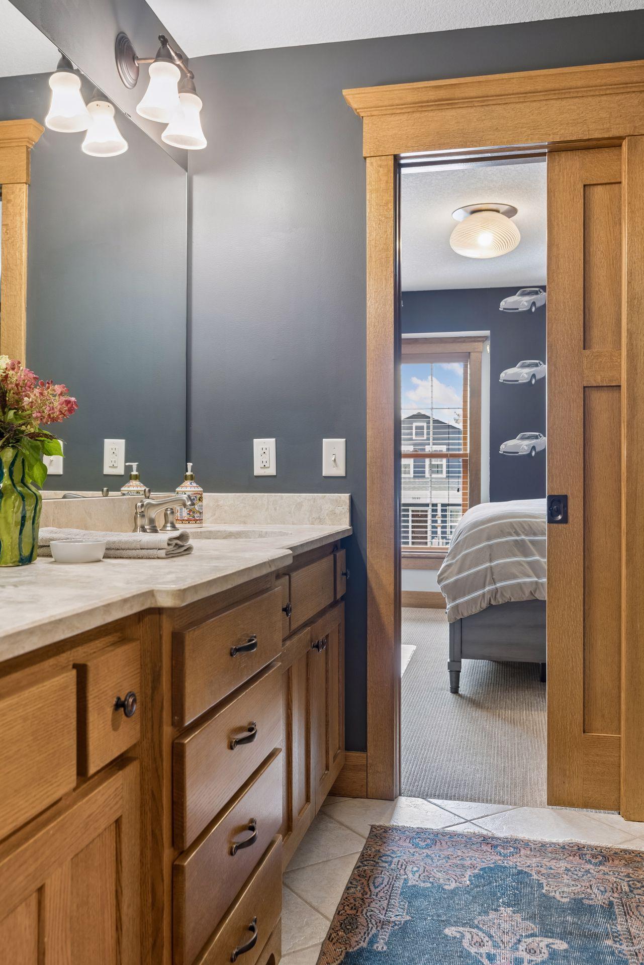 Bathroom vanity with oak cabinets and stone counter beside a doorway to a bedroom.