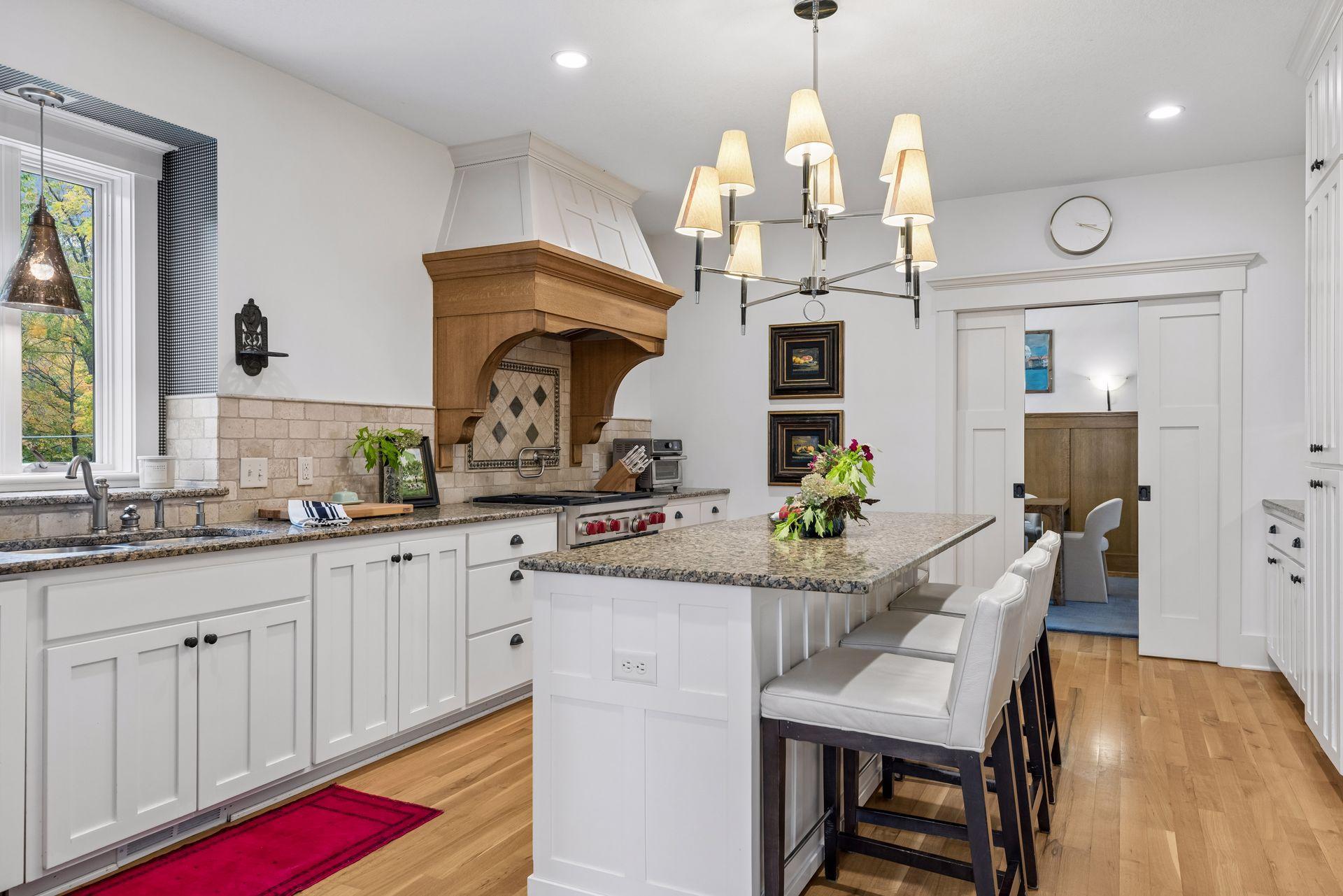 Kitchen with a large granite island, white cabinets, and a prominent wood range hood.