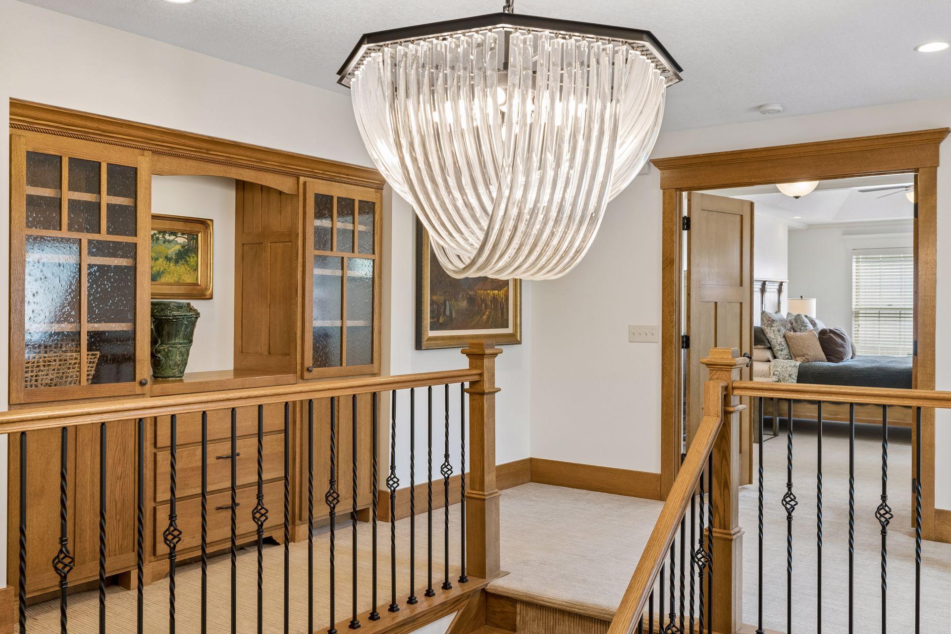 Upper landing with wood railings and built-ins, dominated by a large crystal chandelier.