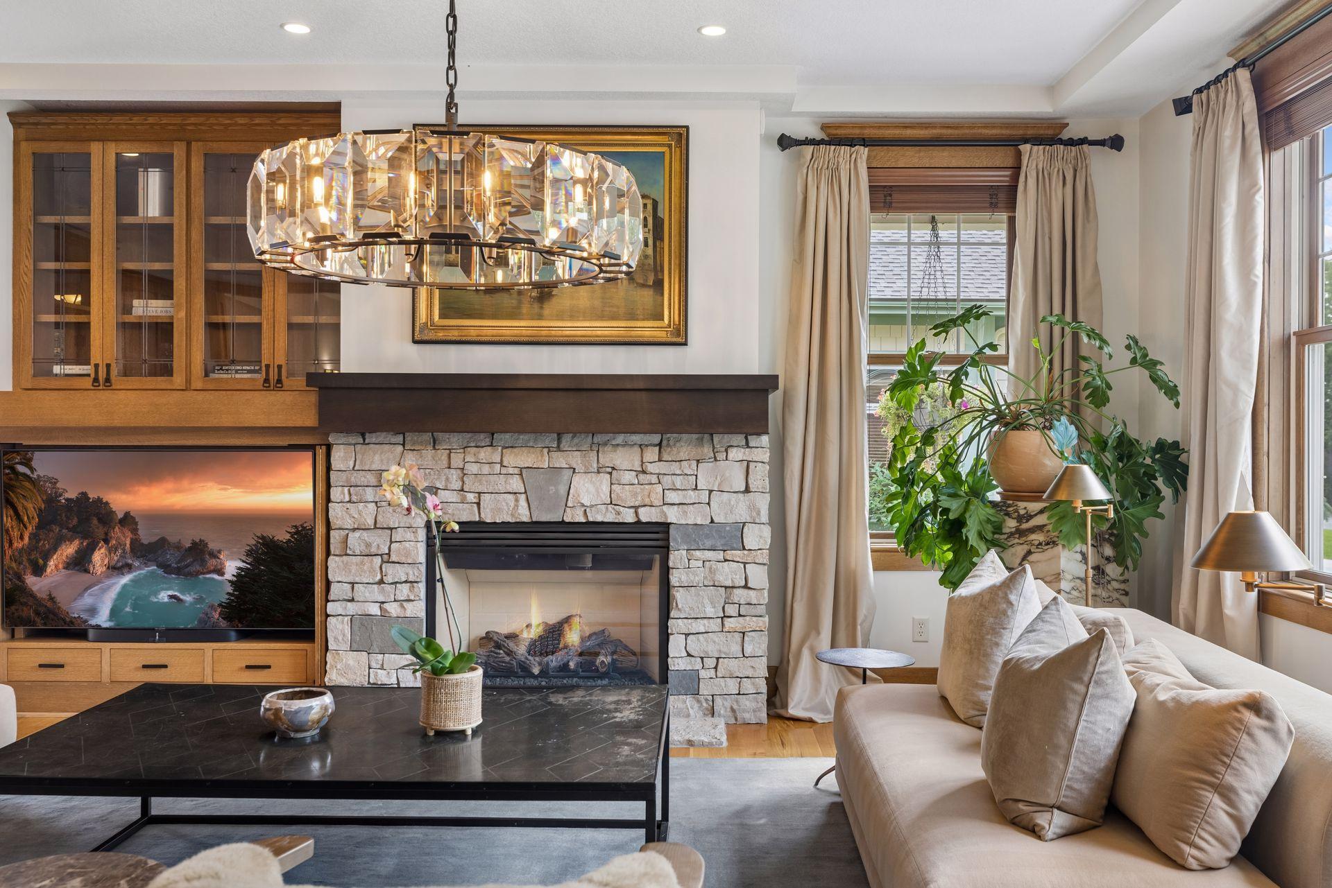 Living room with a stone fireplace, built-in cabinetry, crystal chandelier, and large windows.