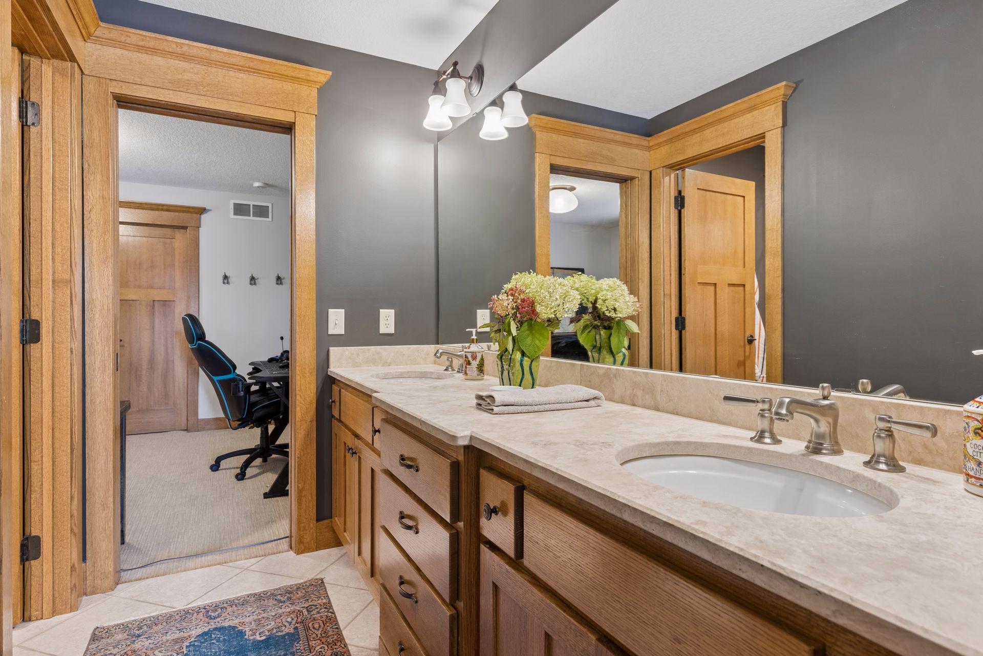 Bathroom vanity with double sinks, light stone counters, wood cabinetry, and a large mirror.