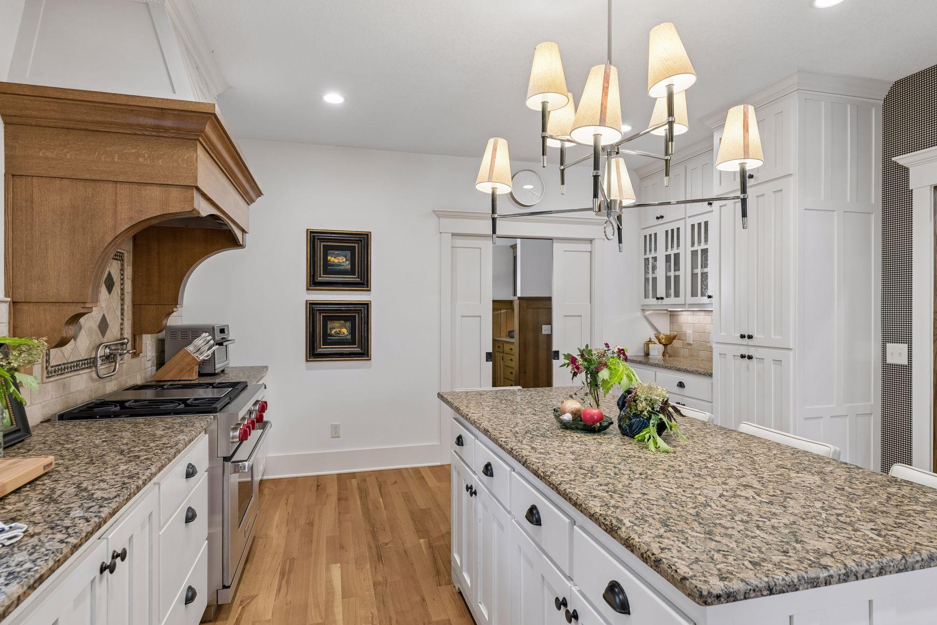 Kitchen with a large granite island, white cabinetry, and a distinctive wood range hood.