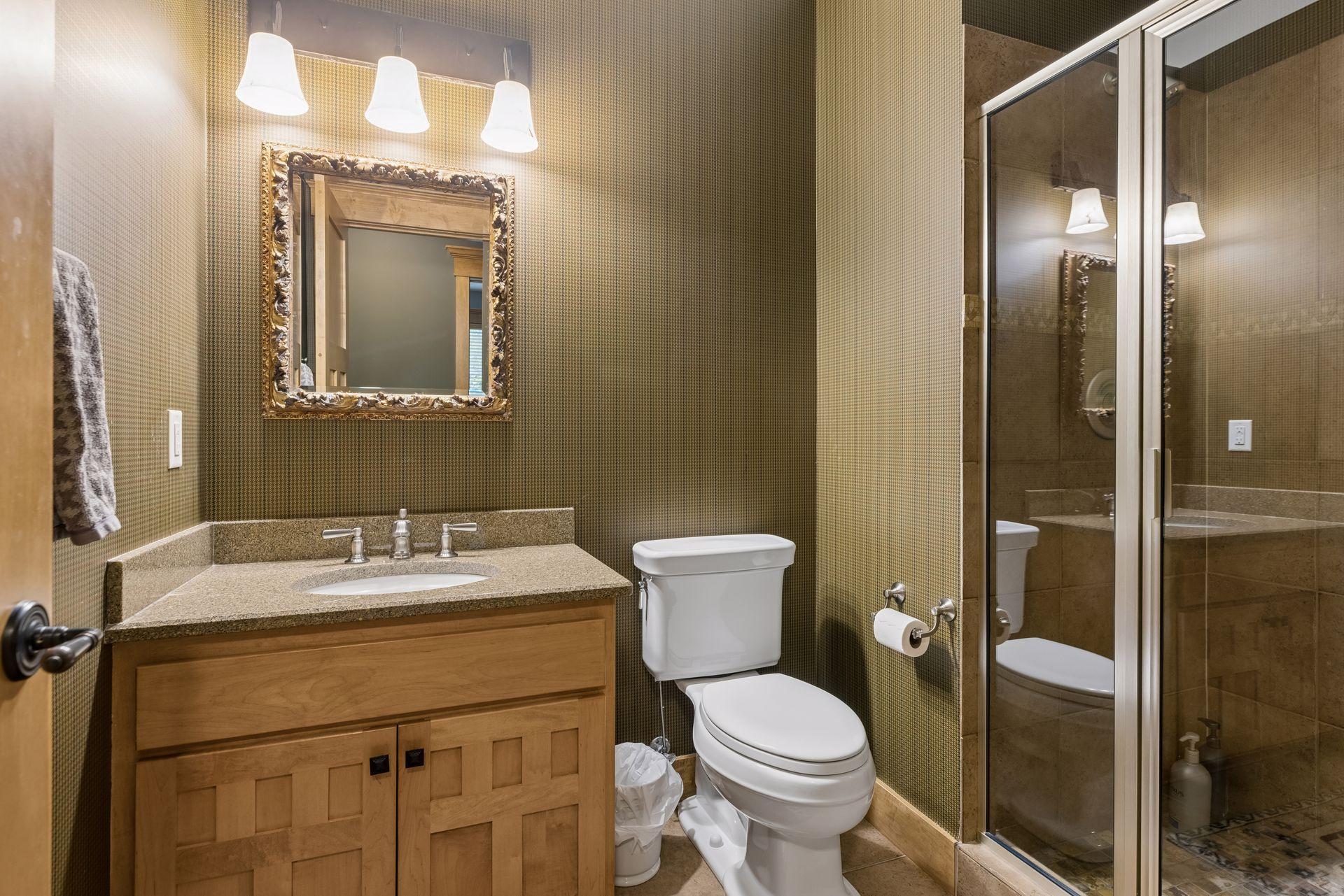 Bathroom with a wood vanity, ornate mirror, and glass-enclosed shower.