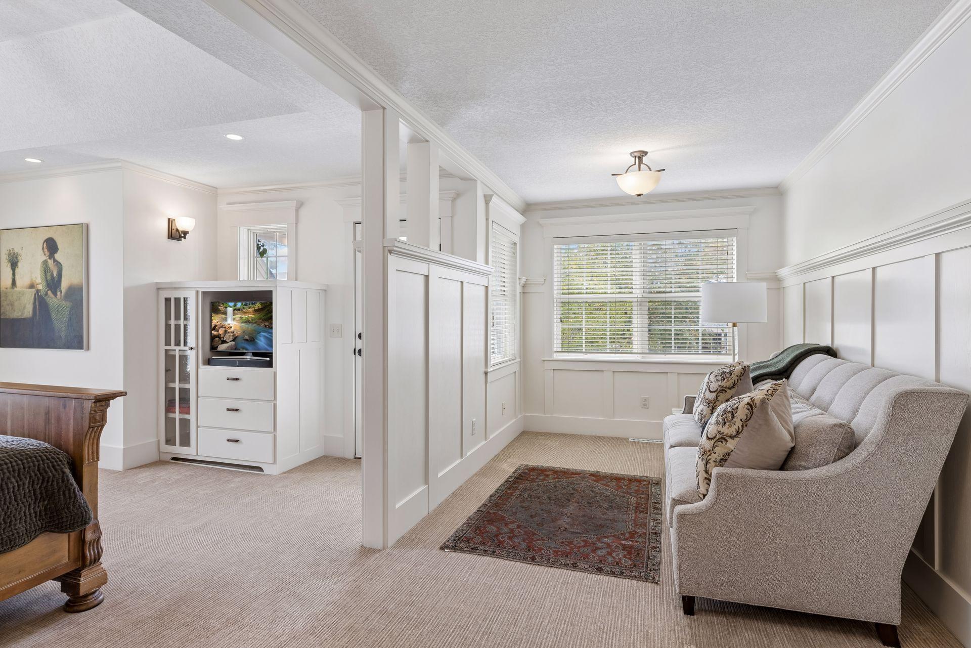 Bright living room with a gray sofa, built-in TV cabinet, white paneling, and large window.