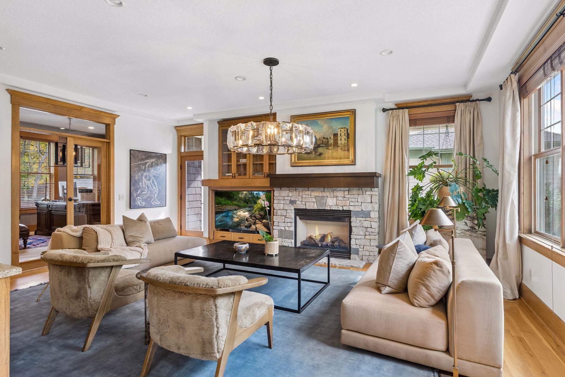 Living room with a stone fireplace, crystal chandelier, and large windows.