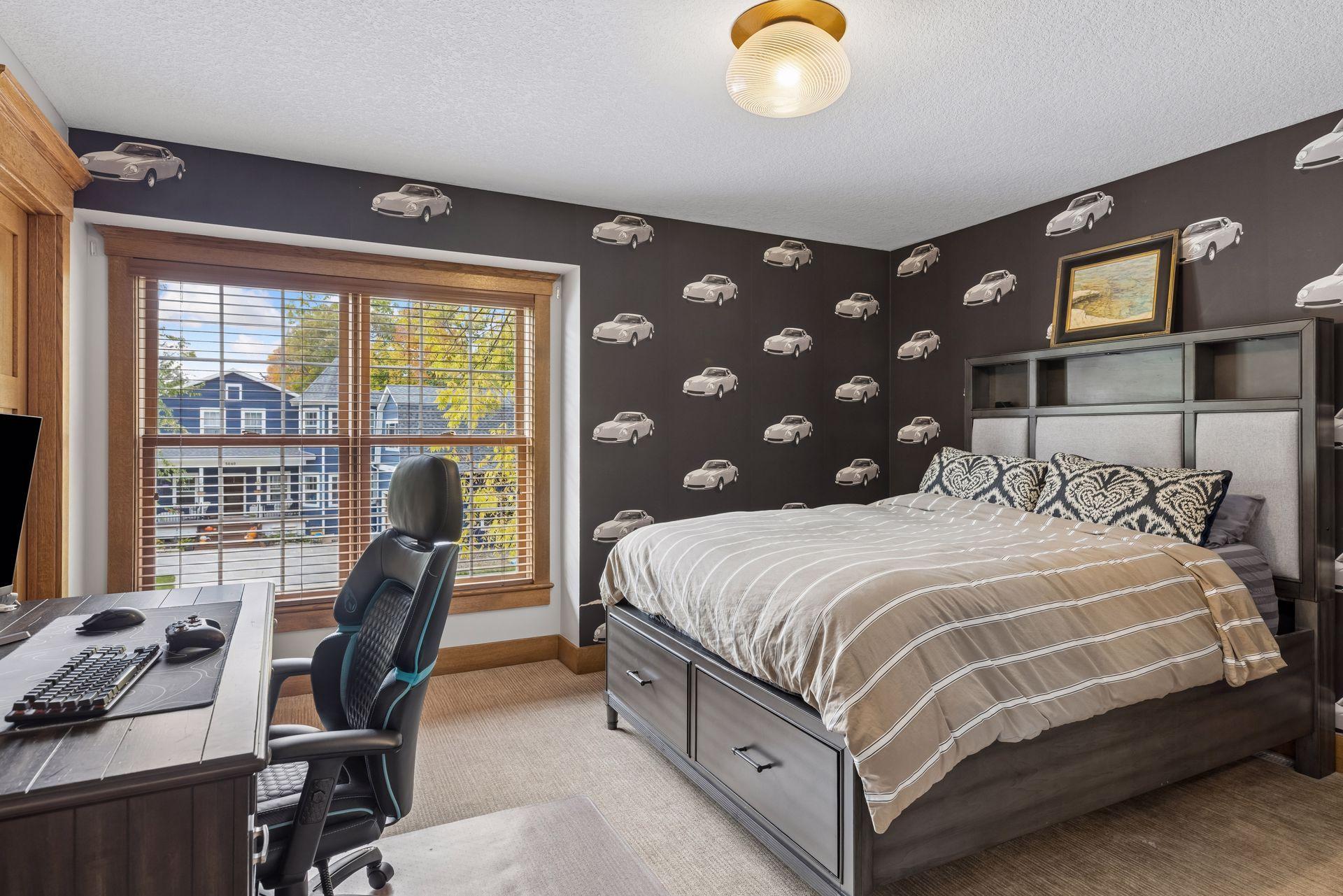 Bedroom with sports car wallpaper, a large bed, and a desk beside a wide window.