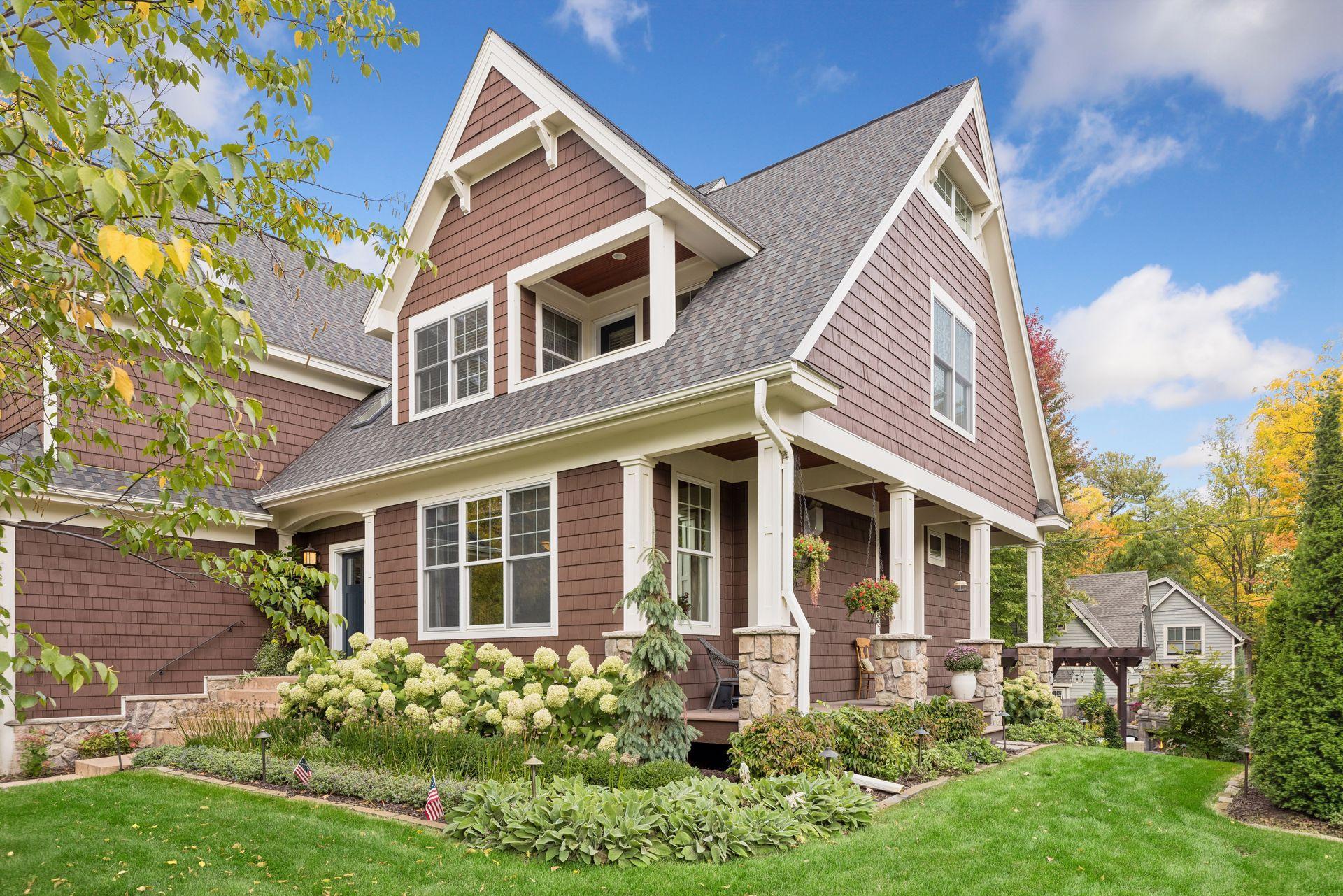 Two-story shingle-sided home with steep gables, a stone-pillared porch, and autumn landscaping.