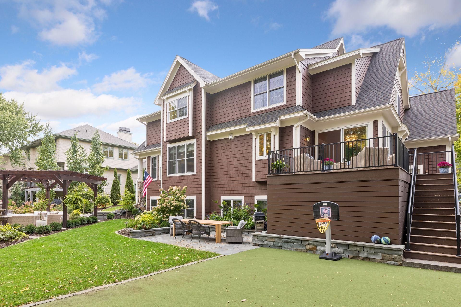 Brown shingle-sided house with raised deck, landscaped yard, pergola, and basketball court.