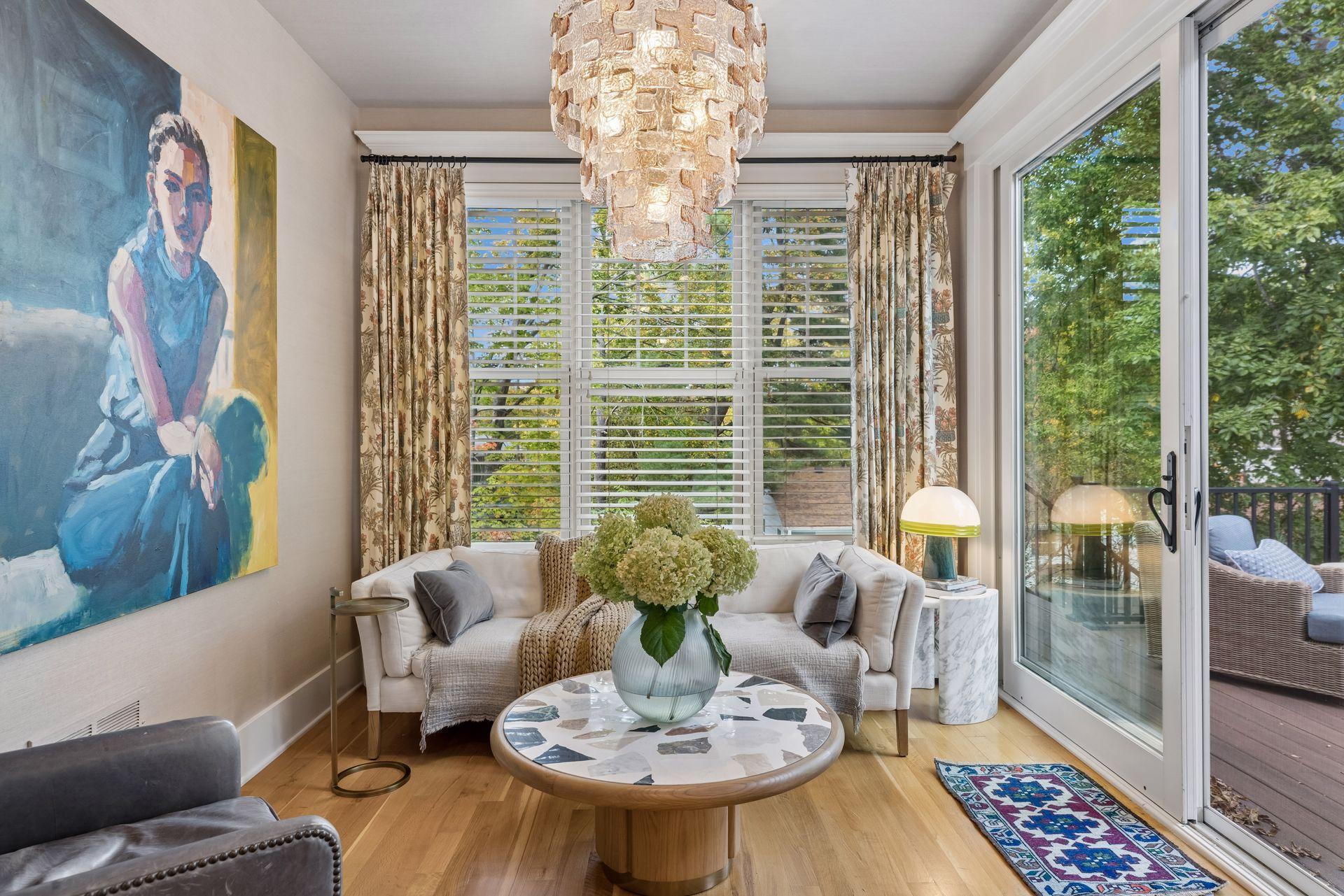 Living room with a white sofa, large abstract painting, and glass doors overlooking leafy trees.