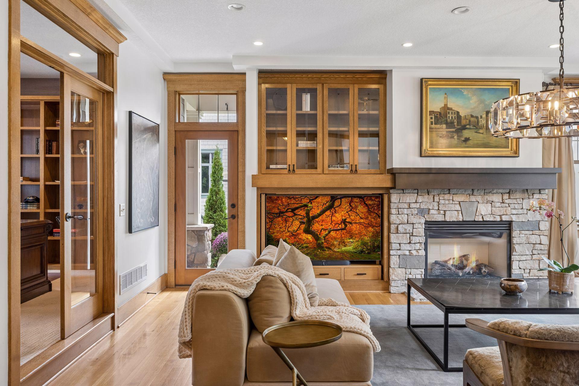 Living room with a stone fireplace, wood built-ins, and television displaying an autumn landscape.