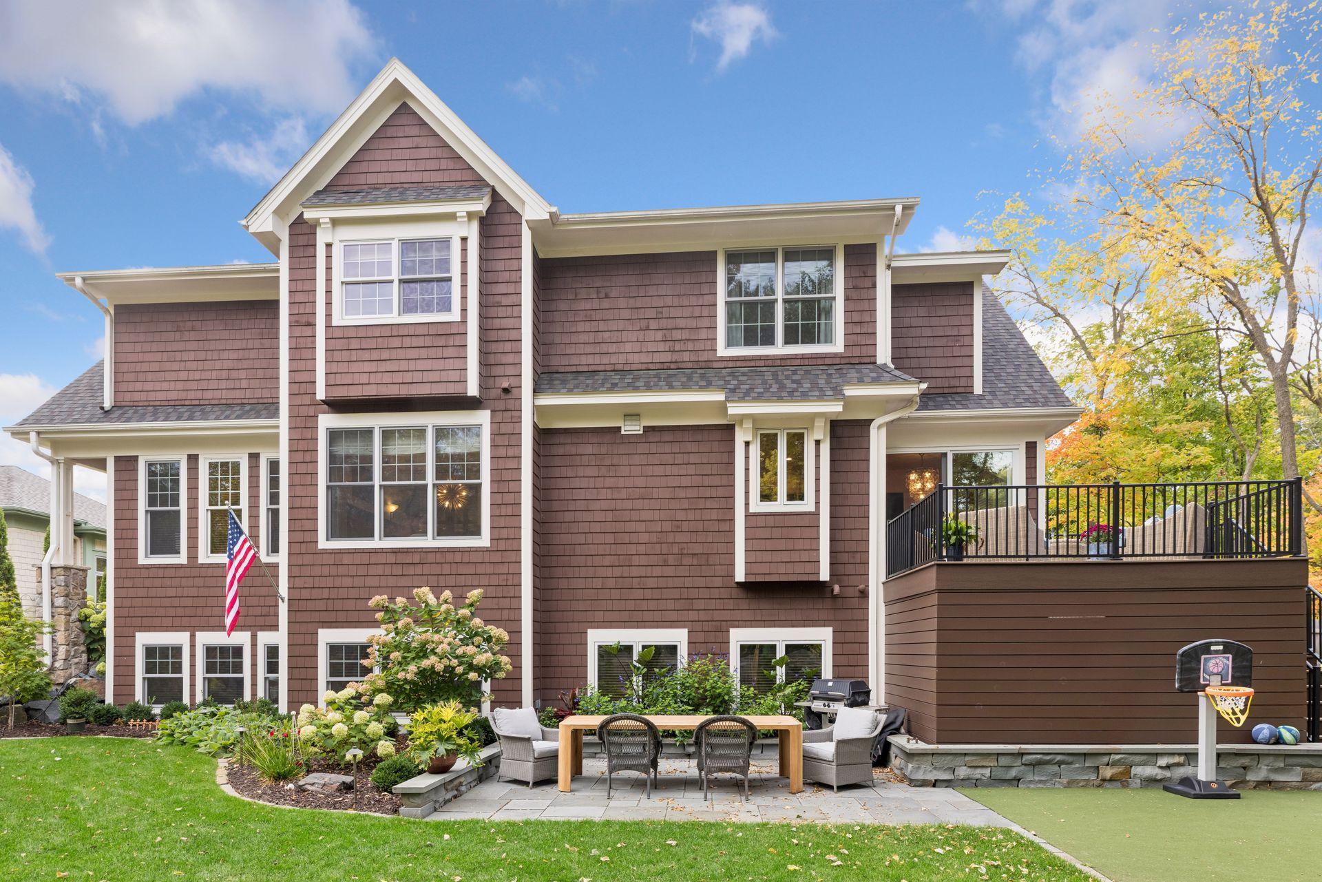 Home’s brown-shingled rear exterior with raised deck, furnished patio, and basketball hoop.