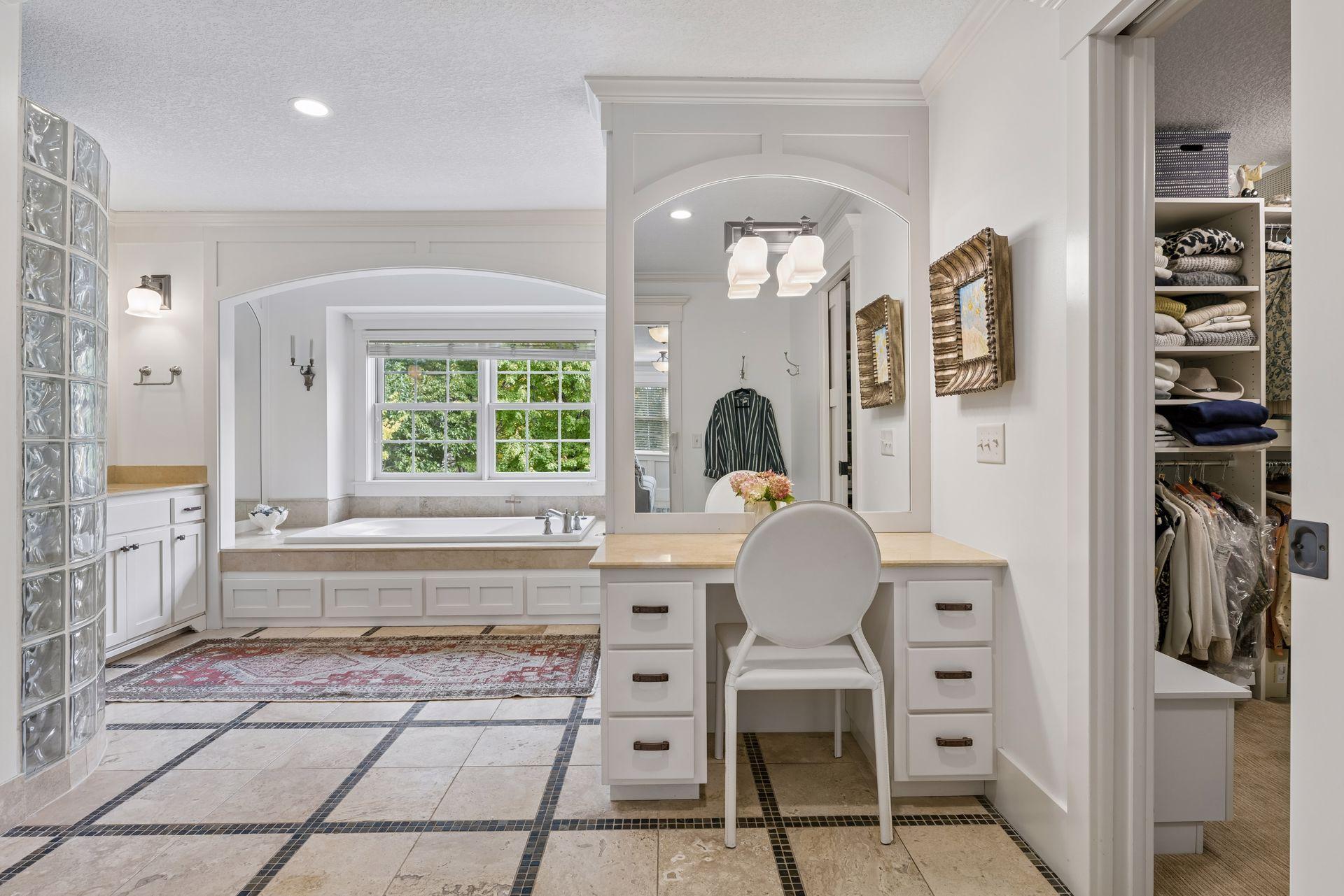 Bathroom with a soaking tub beneath a large window and a white vanity beside an open walk-in closet.