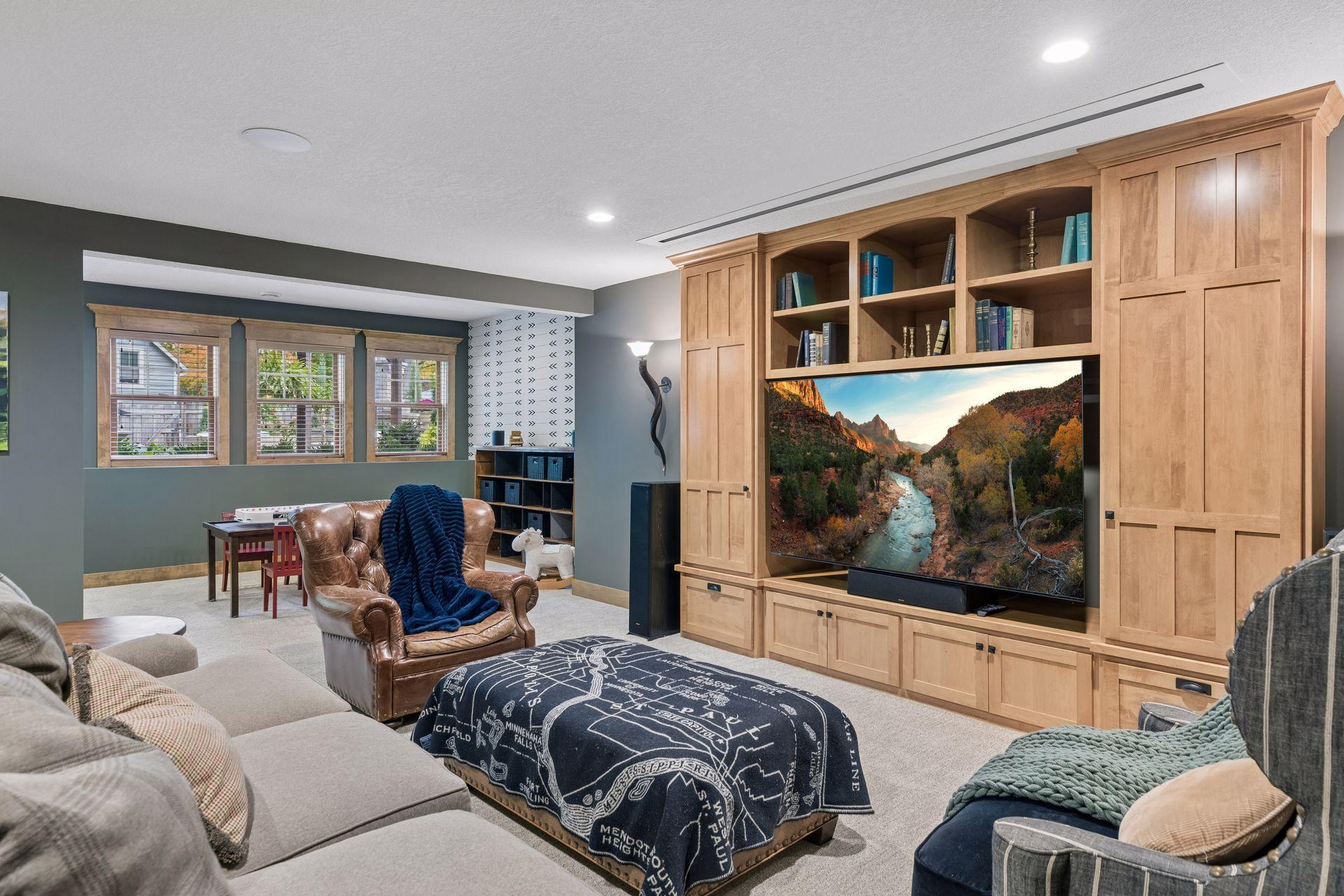 Furnished family room with a built-in wood entertainment center, large television, and seating around a patterned ottoman.
