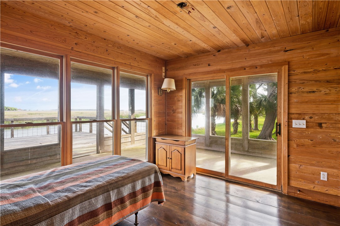 Wood-paneled bedroom with a striped bedspread and broad windows overlooking a deck, palms, and marsh water.