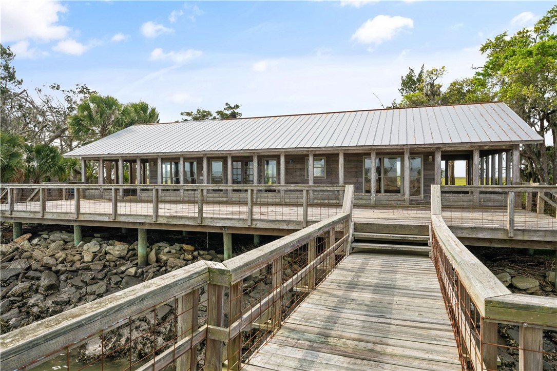Coastal house with a long raised deck, reached by a wooden boardwalk over rocky tidal ground.