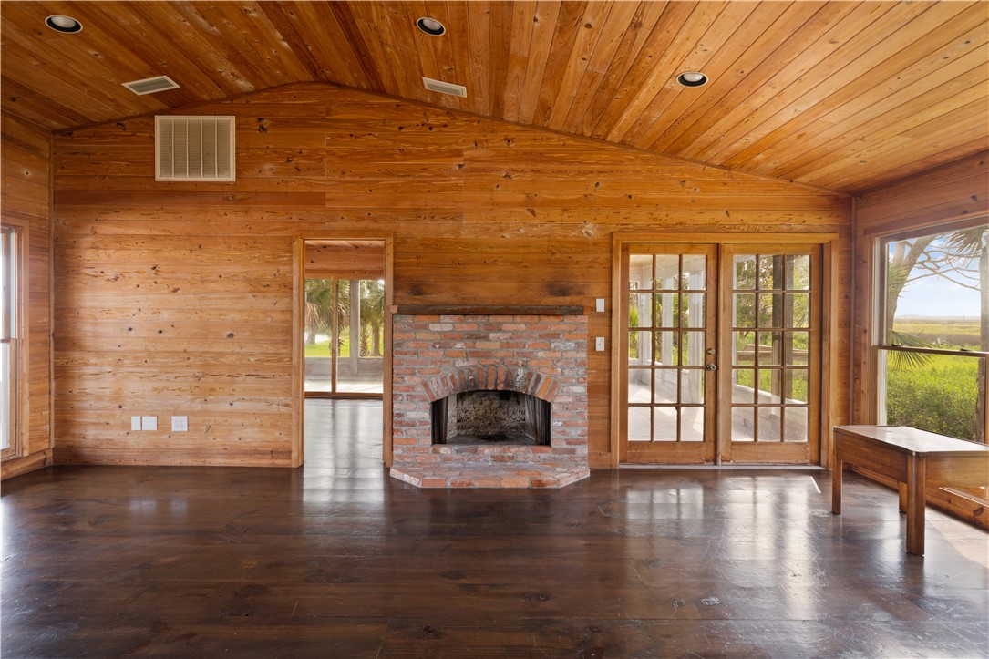 Living room with a vaulted wood ceiling, brick fireplace, and French doors opening to greenery.