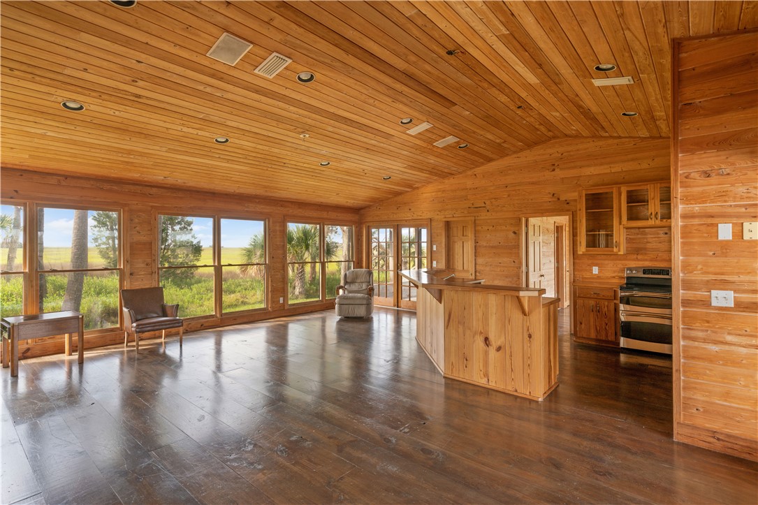 Wood-paneled open-plan kitchen and living area with vaulted ceiling, island, and marsh views.