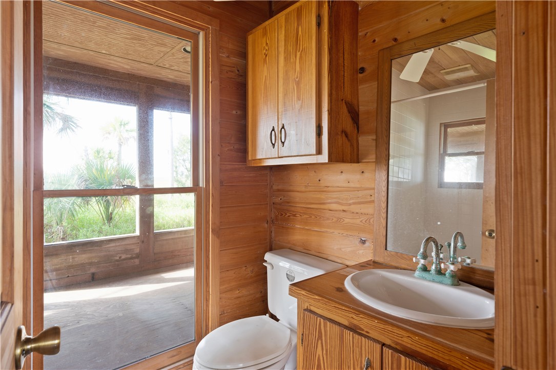 Wood-paneled bathroom with a white vanity sink, toilet, and doorway to a screened porch.