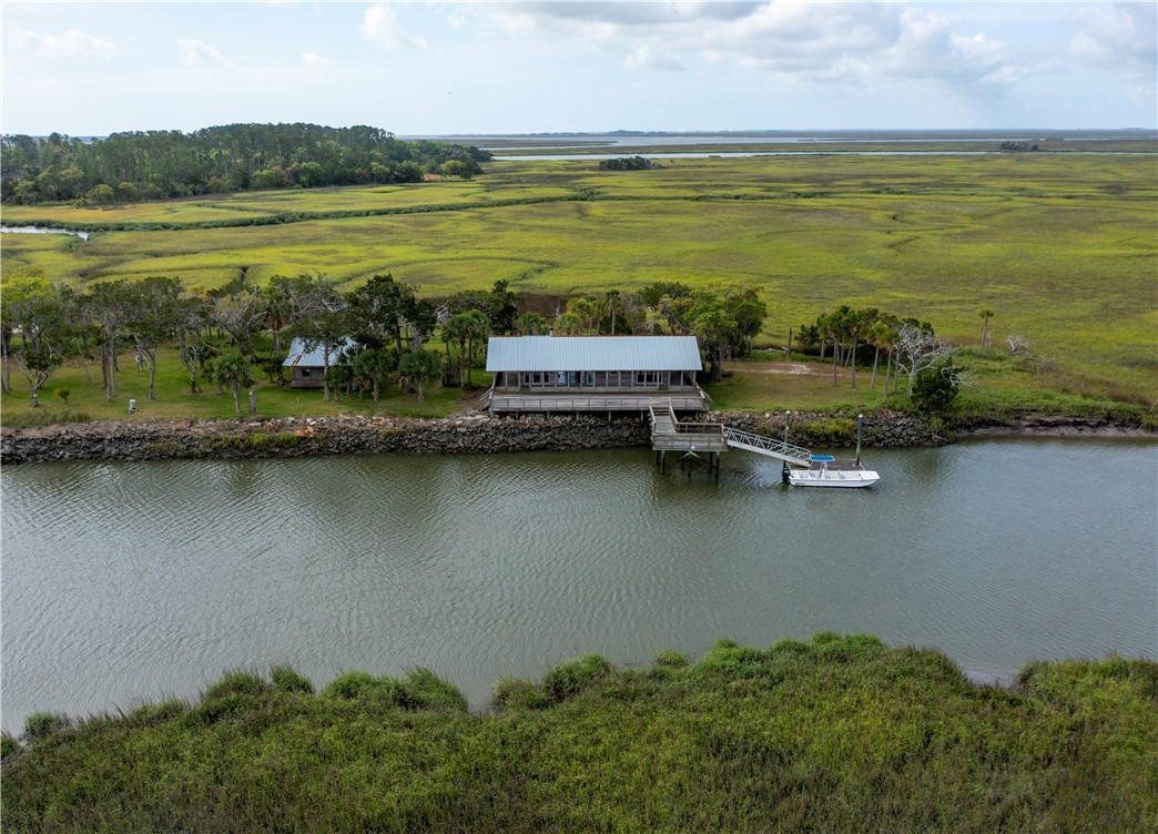 Waterfront building and dock beside a broad green marsh, with a boat tied along the shore.