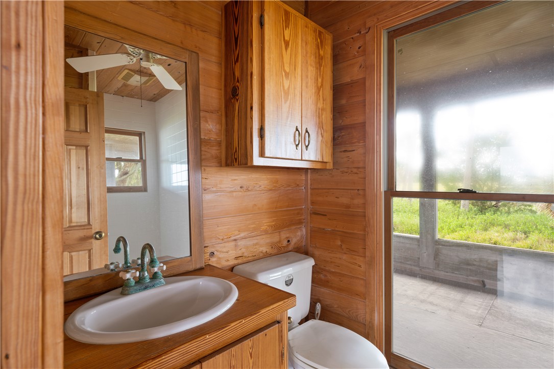 Wood-paneled bathroom with a white sink and toilet beside a large window.